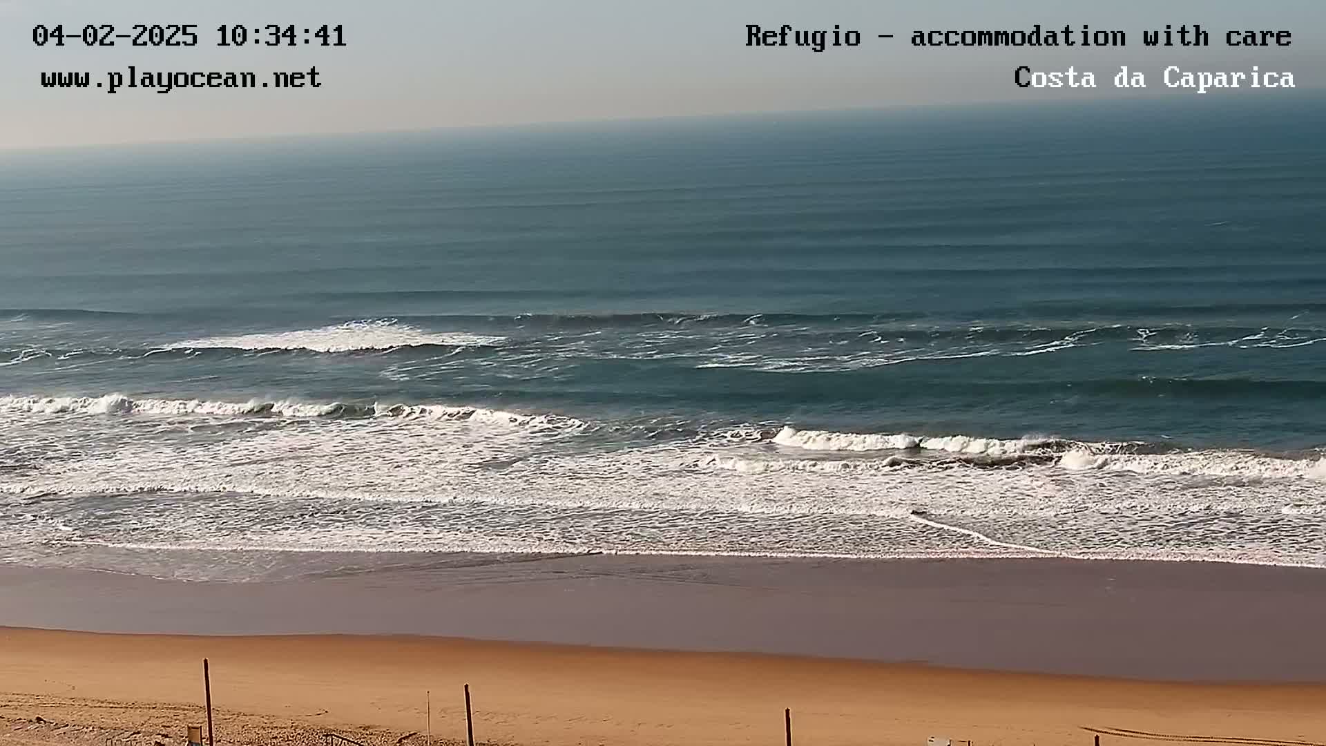 Ocean waves roll onto a sandy beach under a clear sky.