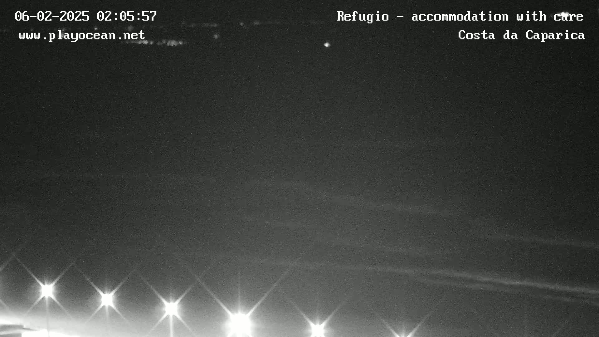 A nighttime, outdoor view shows a dark sky with faint clouds and a line of bright lights at the bottom of the frame.