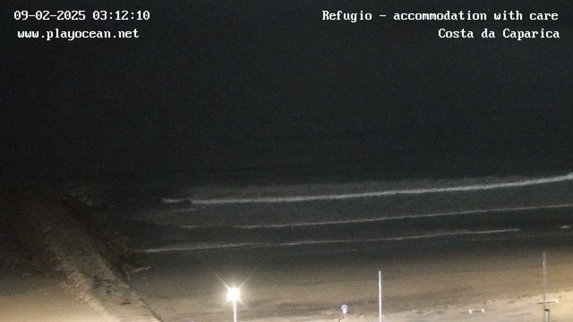 A dark, nighttime view of a beach with gently rolling waves under a clear sky.