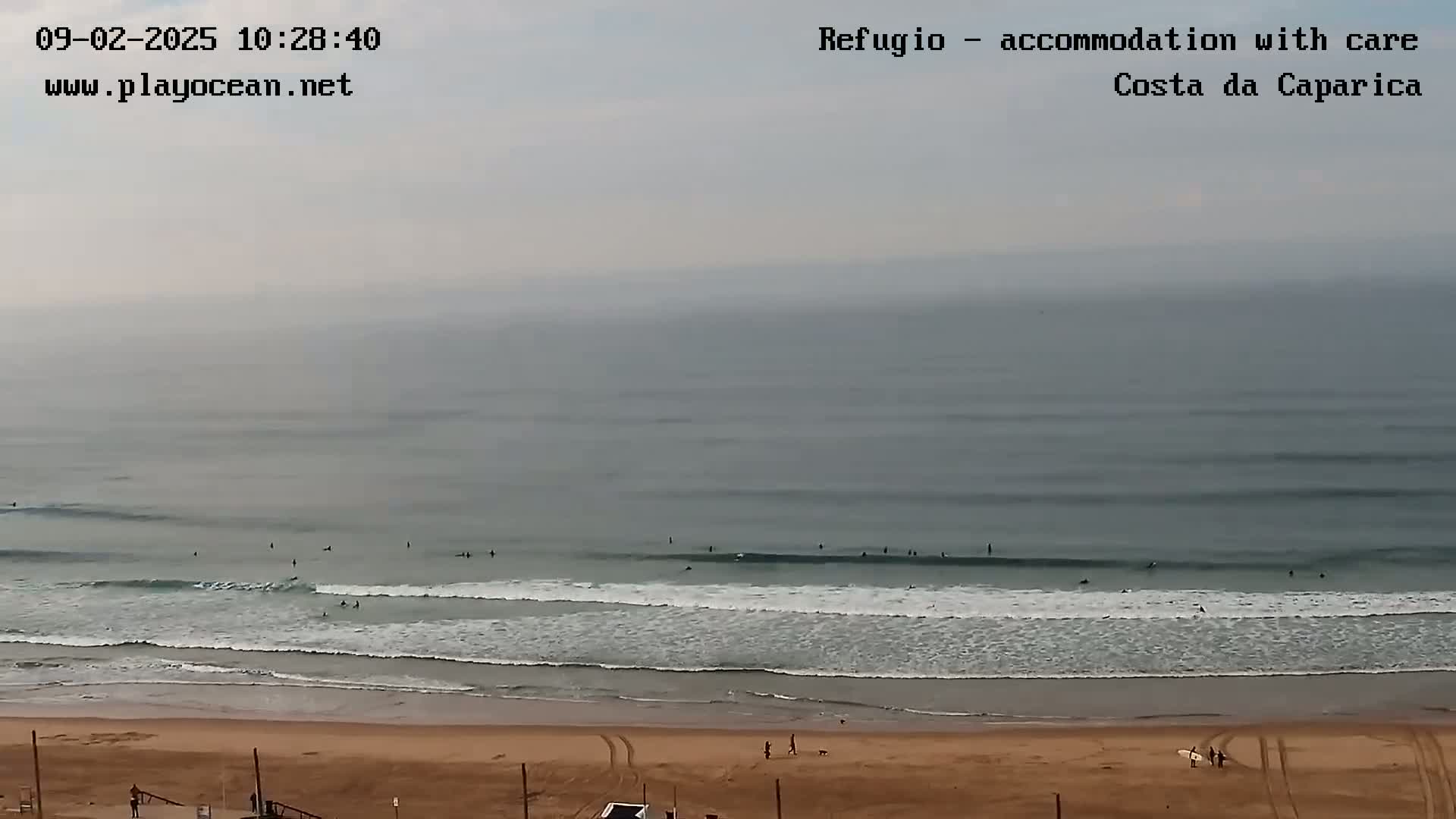 A mostly cloudy day shows several surfers in the ocean waves near a sandy beach.