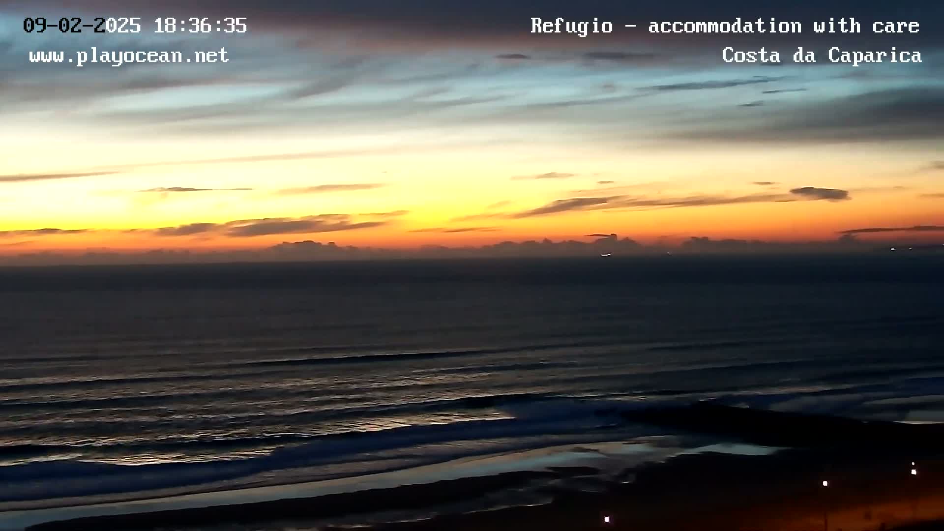 A vibrant sunset over a dark ocean with gently rolling waves on a beach.