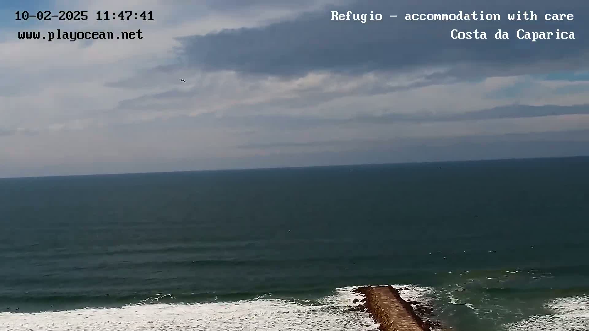 A dark, overcast sky hangs over a dark teal ocean with small waves breaking on a long, narrow jetty.