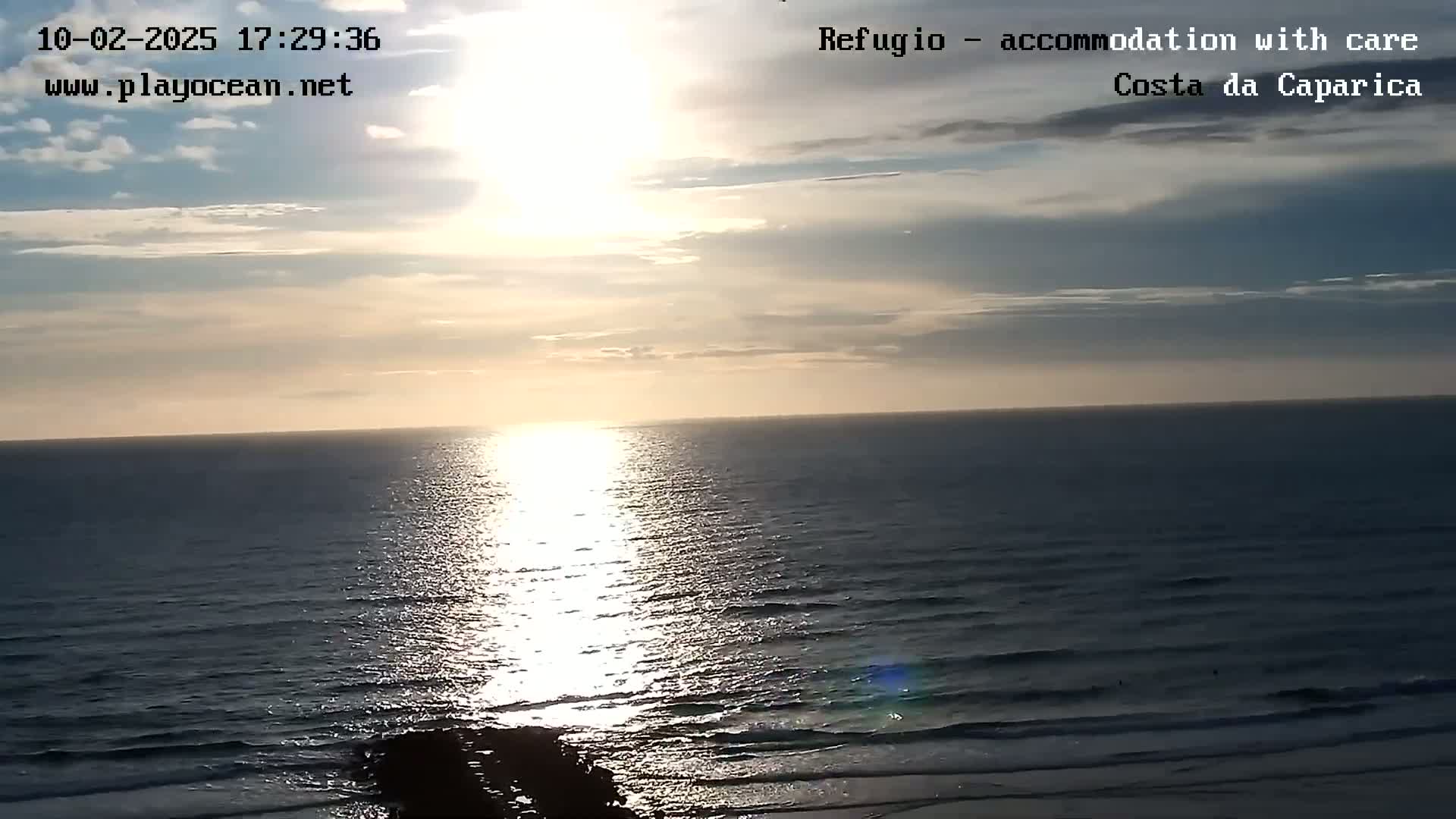 A bright sunset over a calm ocean with a partly cloudy sky.