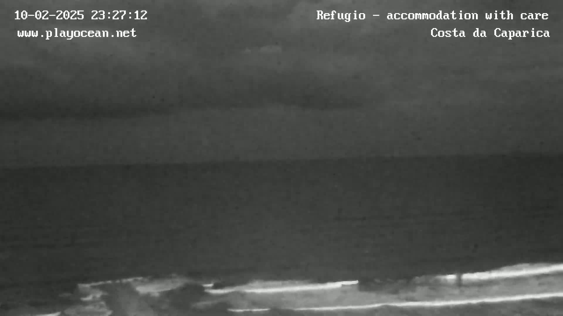 A nighttime, low-light image shows a dark ocean under a cloudy sky, with a dark shoreline visible in the bottom of the frame.
