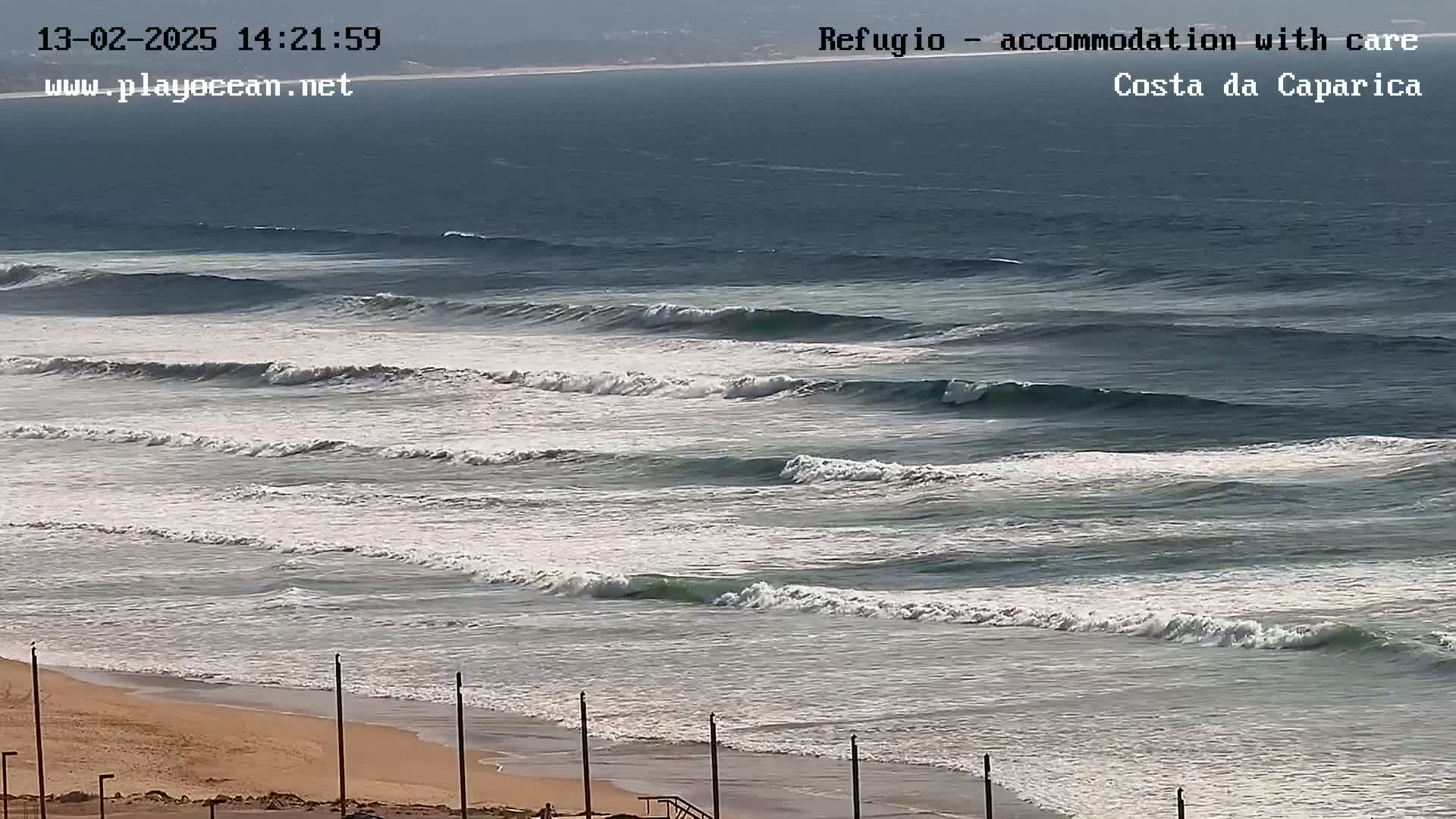 A sandy beach with a calm ocean and several consistent waves breaking.