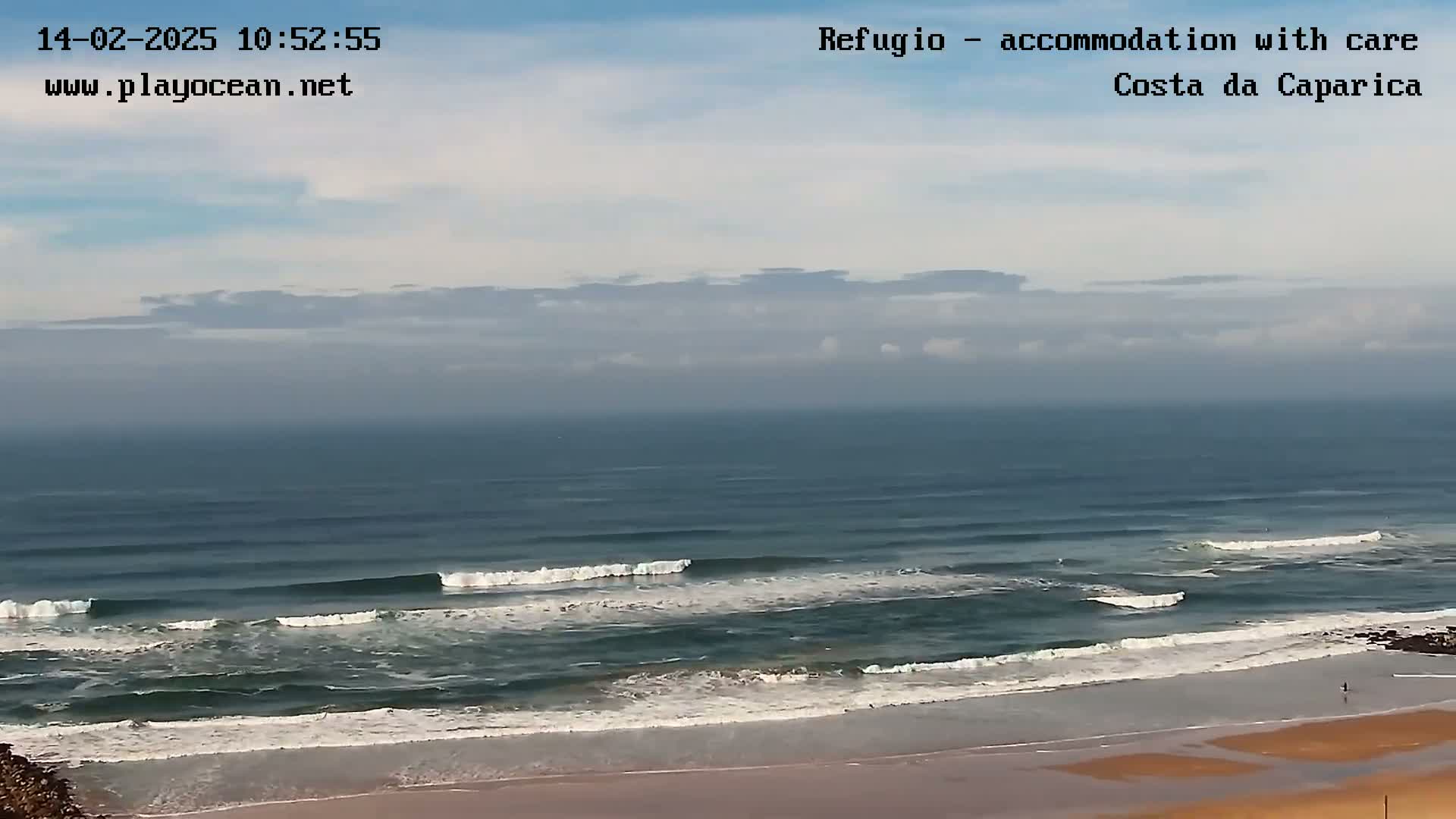 A partly cloudy day shows a view of an ocean beach with several small waves breaking near the shore.
