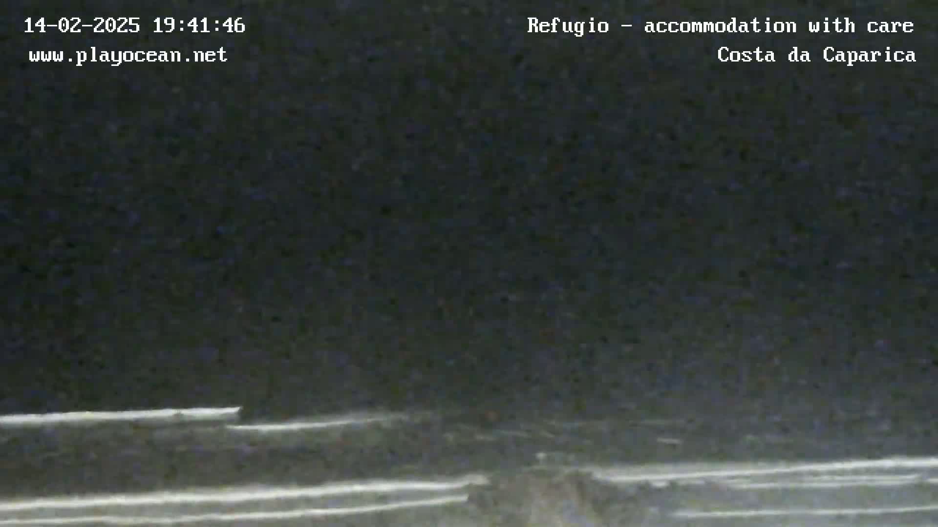 A dark, nighttime coastal scene shows a beach with dark water and faint white lines suggesting waves under a dark sky.