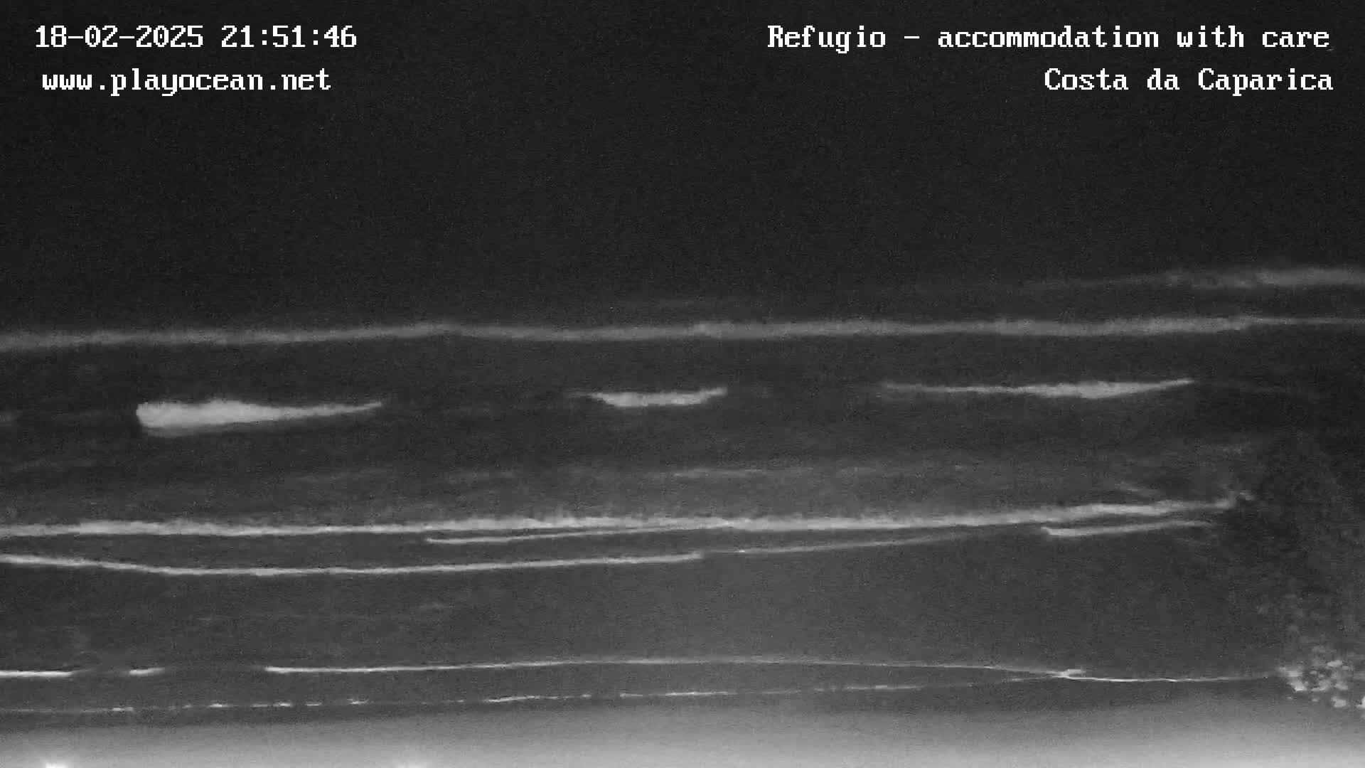A nighttime, low-light image shows a dark ocean with several faint, horizontal lines of white waves or foam visible near the horizon.
