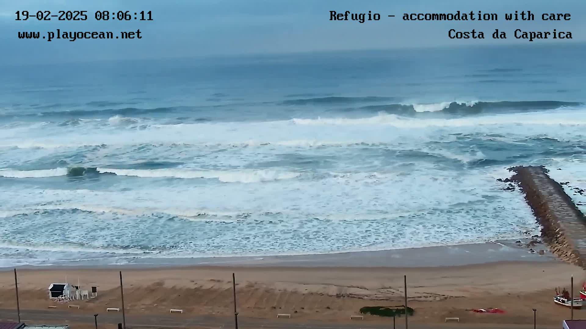 A sandy beach with a rocky jetty extends into a choppy ocean under an overcast sky.