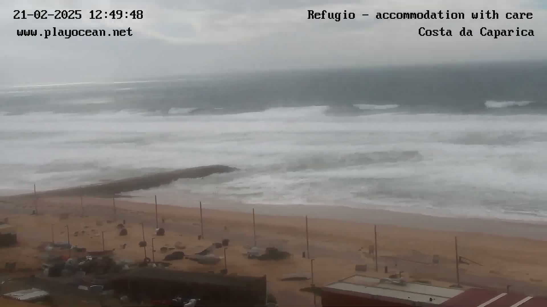 A wide shot shows a beach with overcast skies and large waves crashing on the shore.