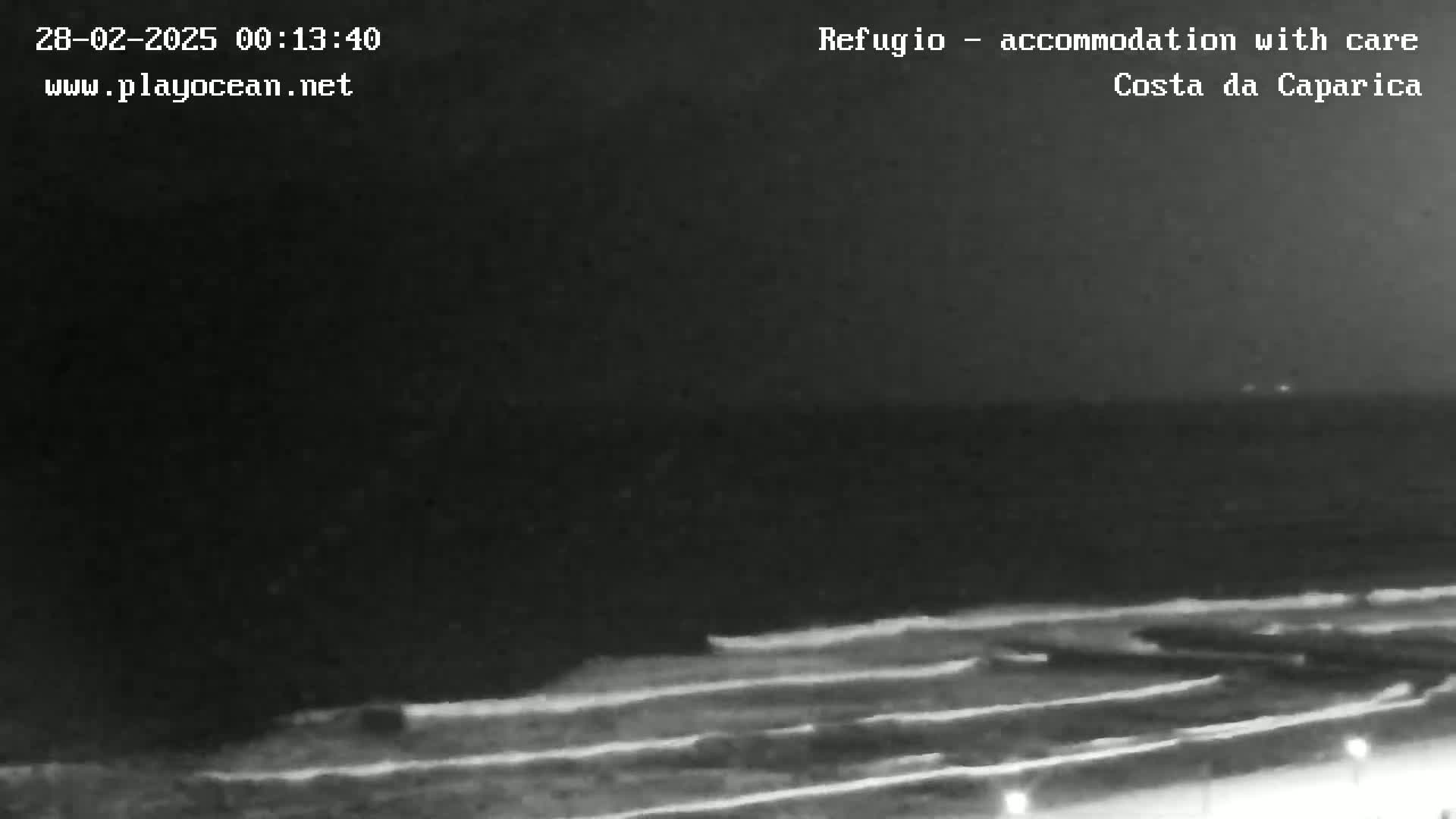 A nighttime, low-light view shows dark ocean waves lapping a shoreline.