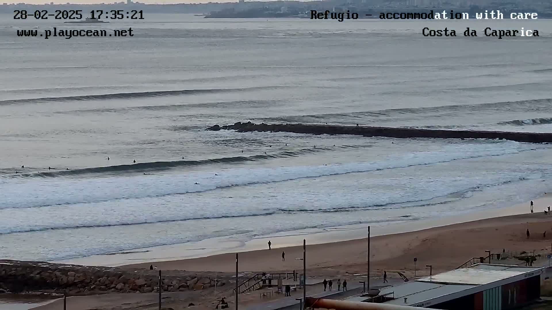 A long, sandy beach with several surfers in the ocean under an overcast sky.