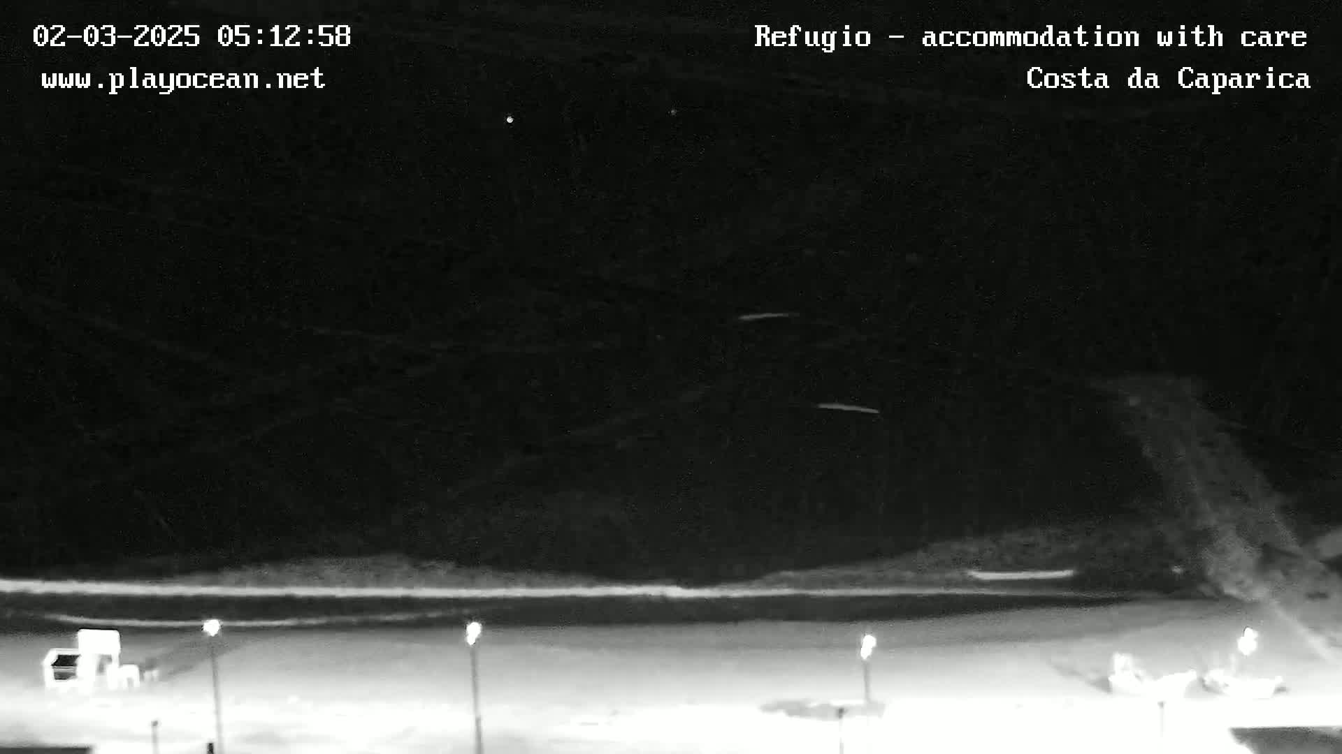 A nighttime, snow-covered landscape is visible, featuring a flat expanse of land with sparsely placed lights and what appears to be a building in the bottom left corner, under a dark sky with some faint streaks possibly indicating light snow or rain.