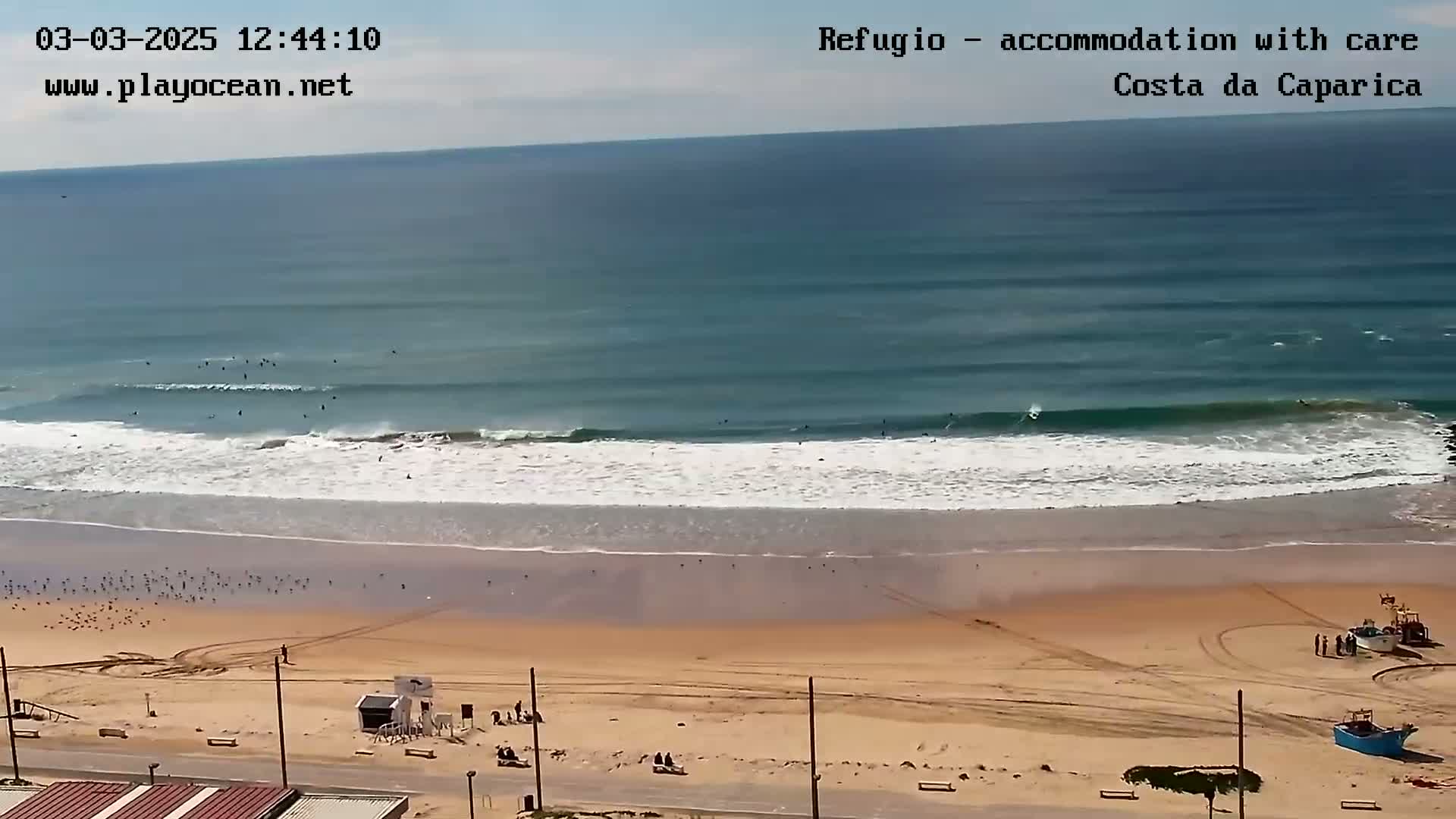 A sandy beach with many surfers in the ocean under a mostly clear sky.