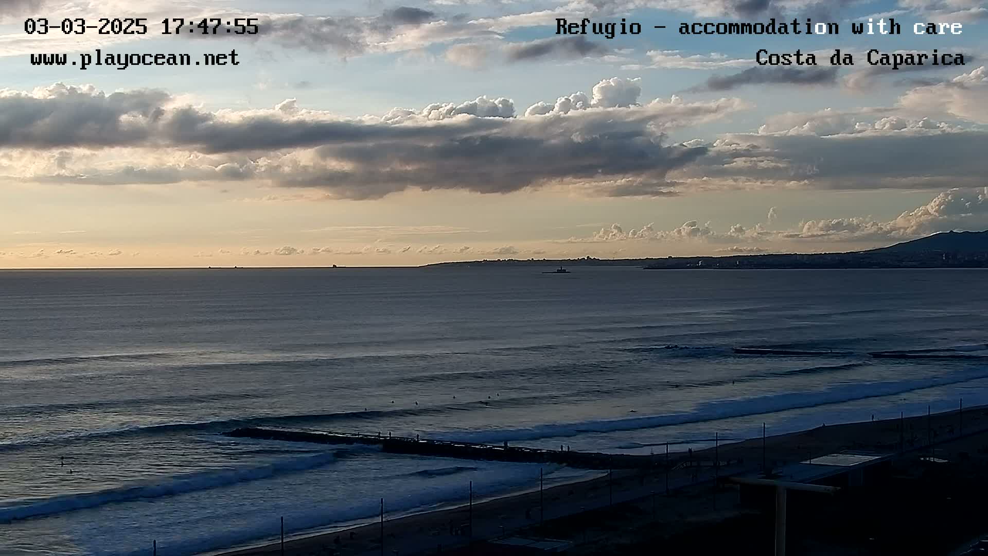 A partly cloudy sunset over a beach with waves rolling into shore.
