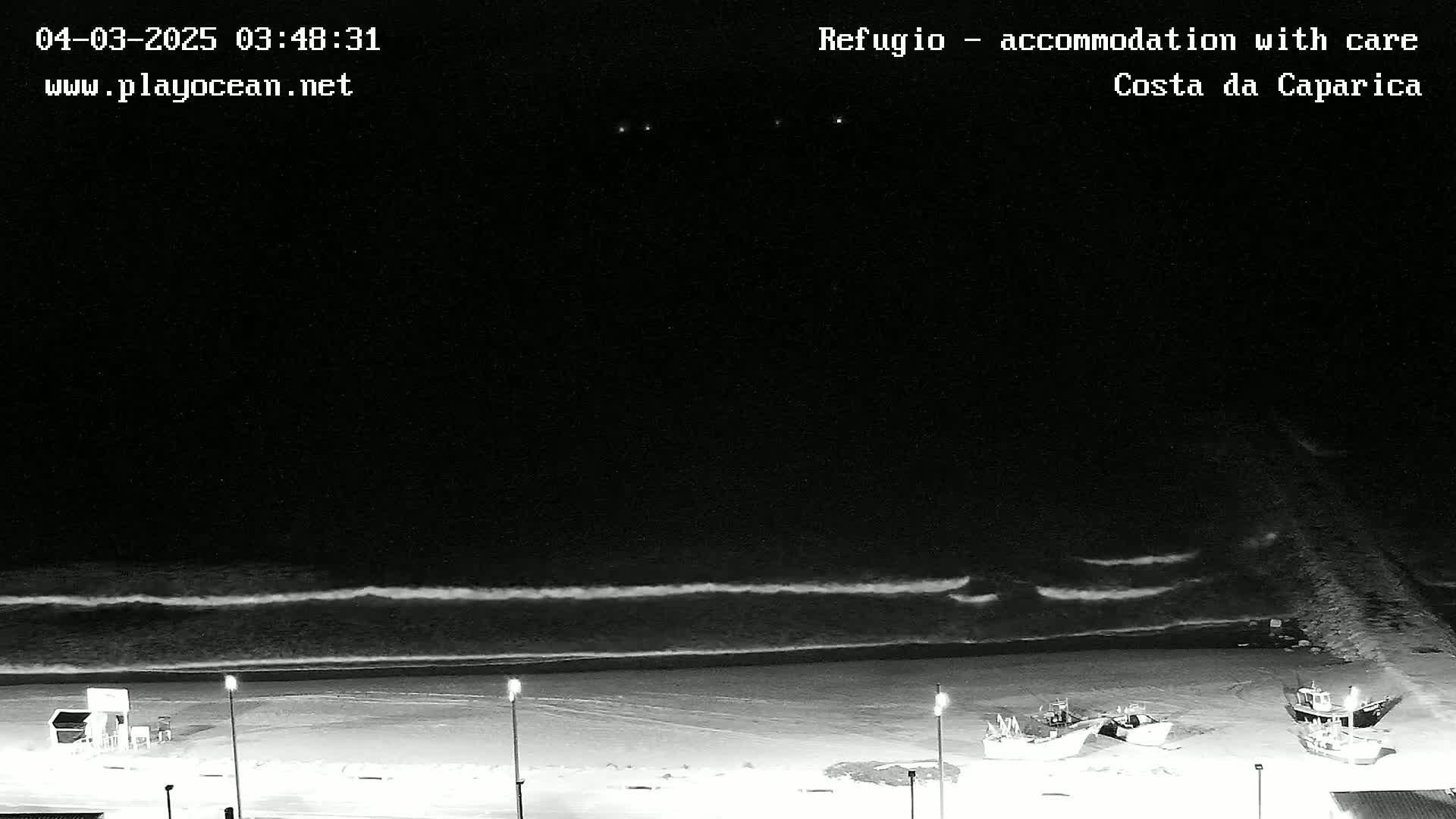 A nighttime beach scene shows gentle waves lapping the shore under a dark sky.