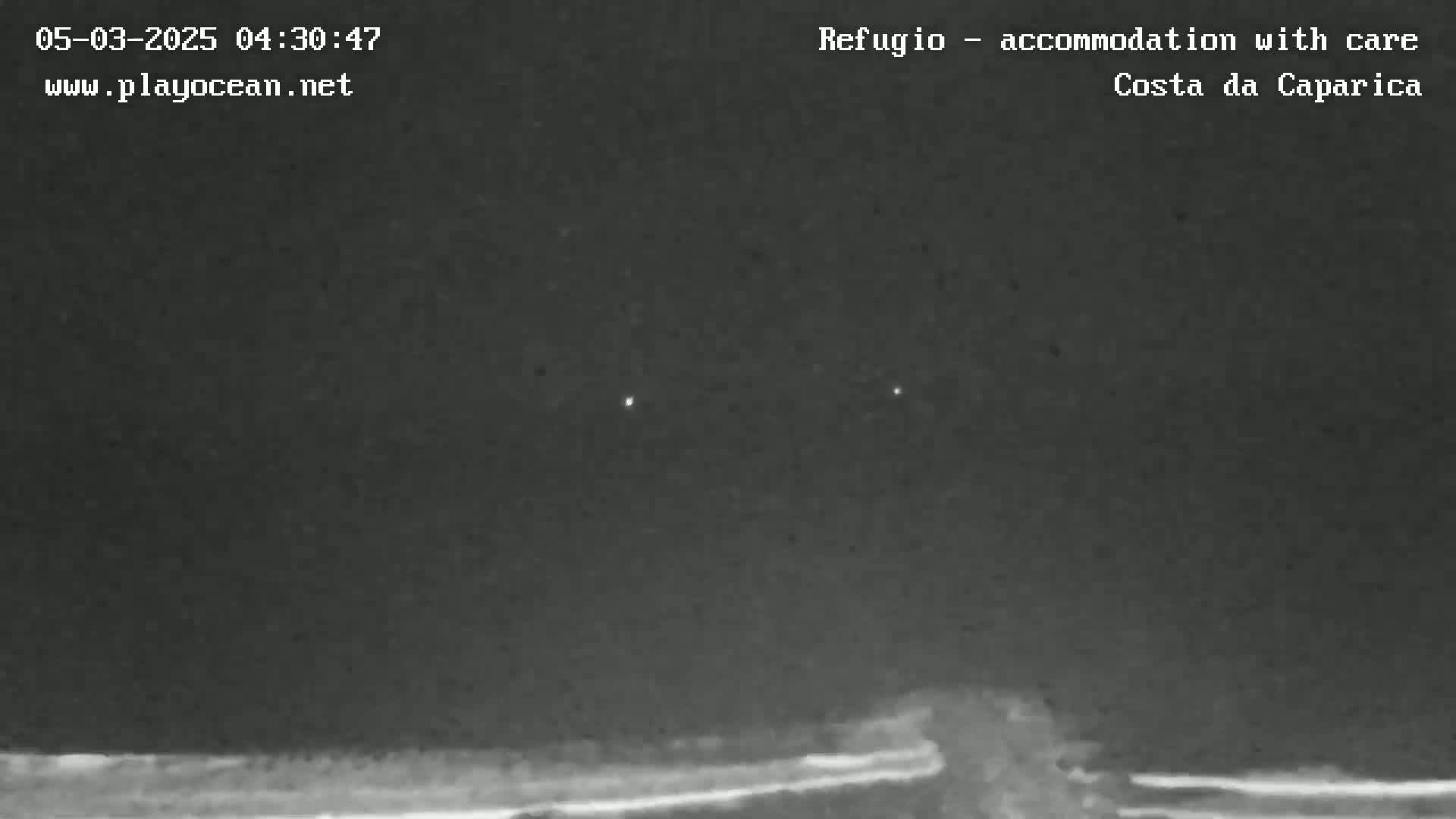 A nighttime, low-light view of a dark horizon with two faint lights visible in the distance.