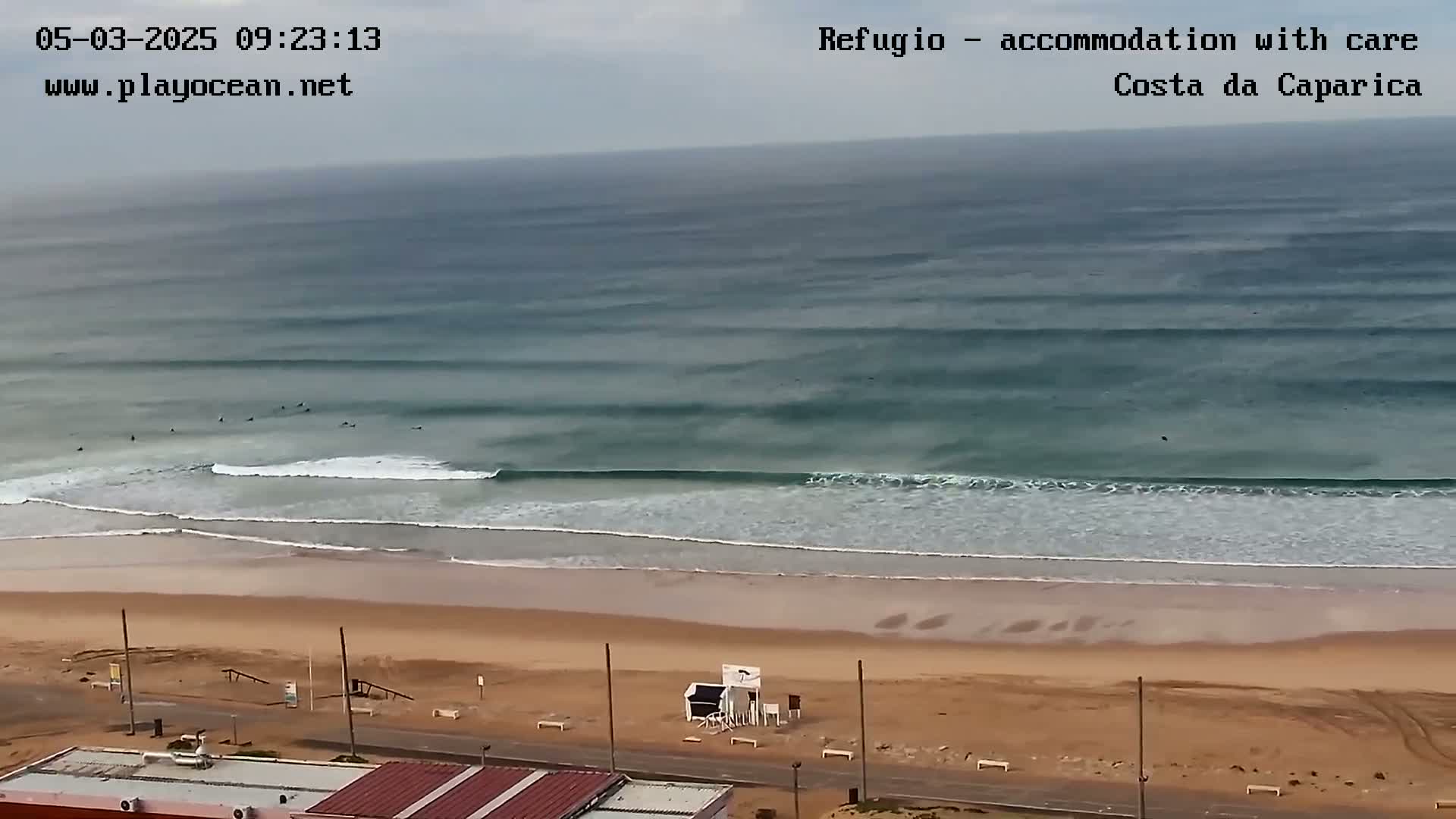 A long sandy beach with several surfers in the ocean under an overcast sky.