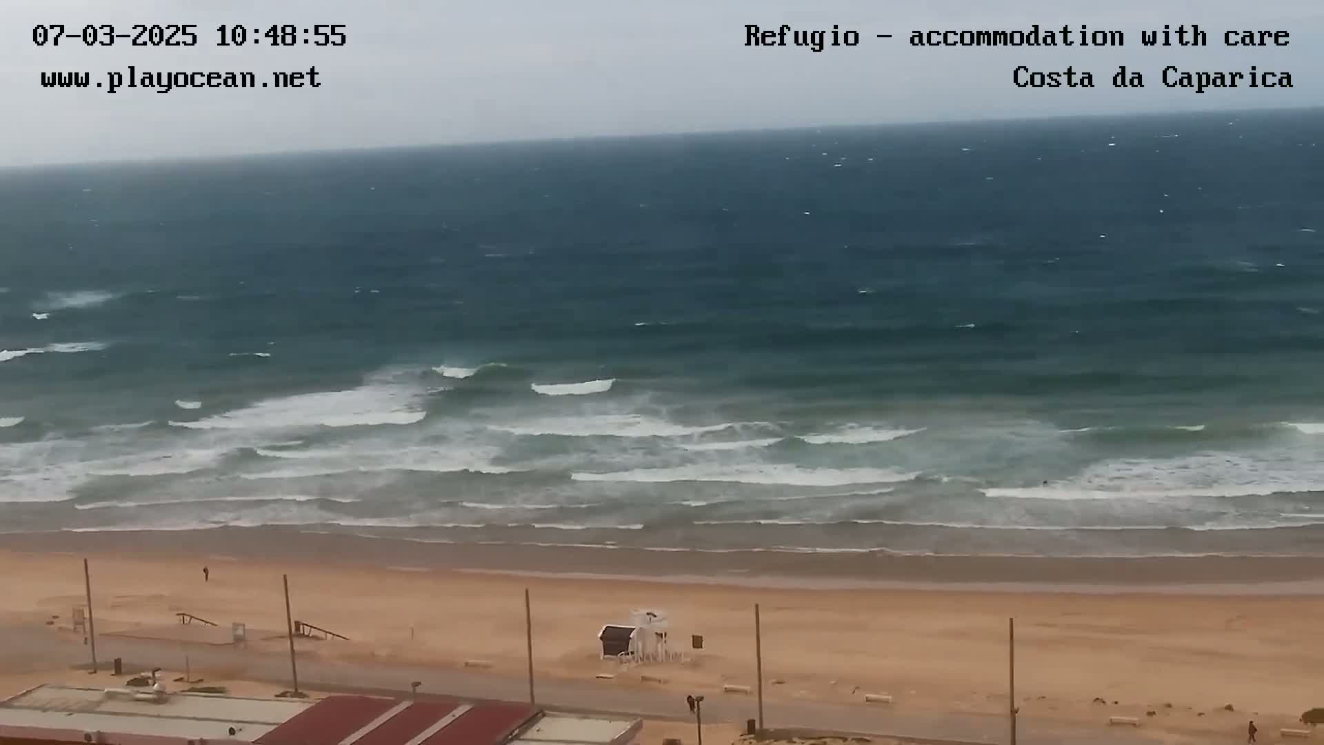A wide shot shows an overcast day at a beach with moderate waves crashing on the shore.