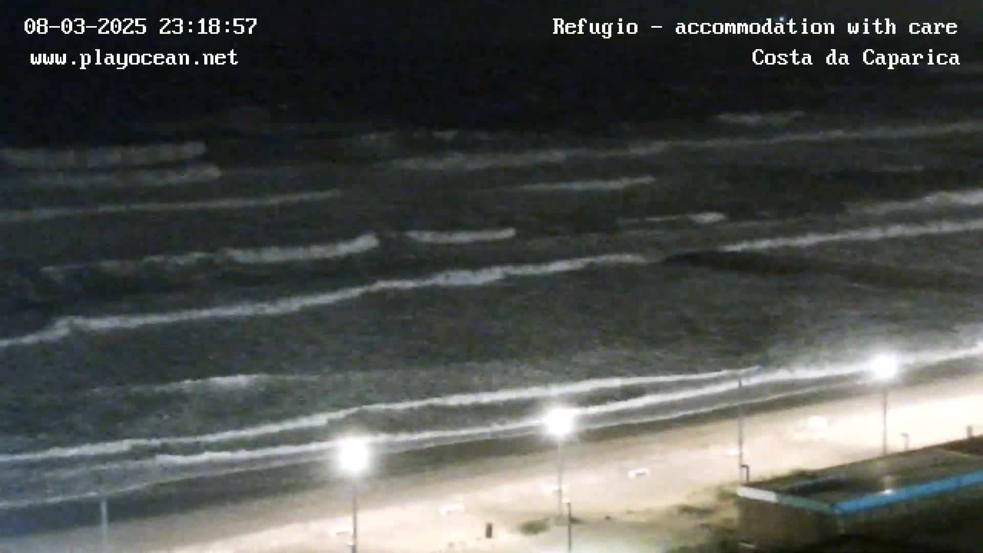 A nighttime view of a beach with moderately sized waves rolling onto the shore under dark, cloudy skies.