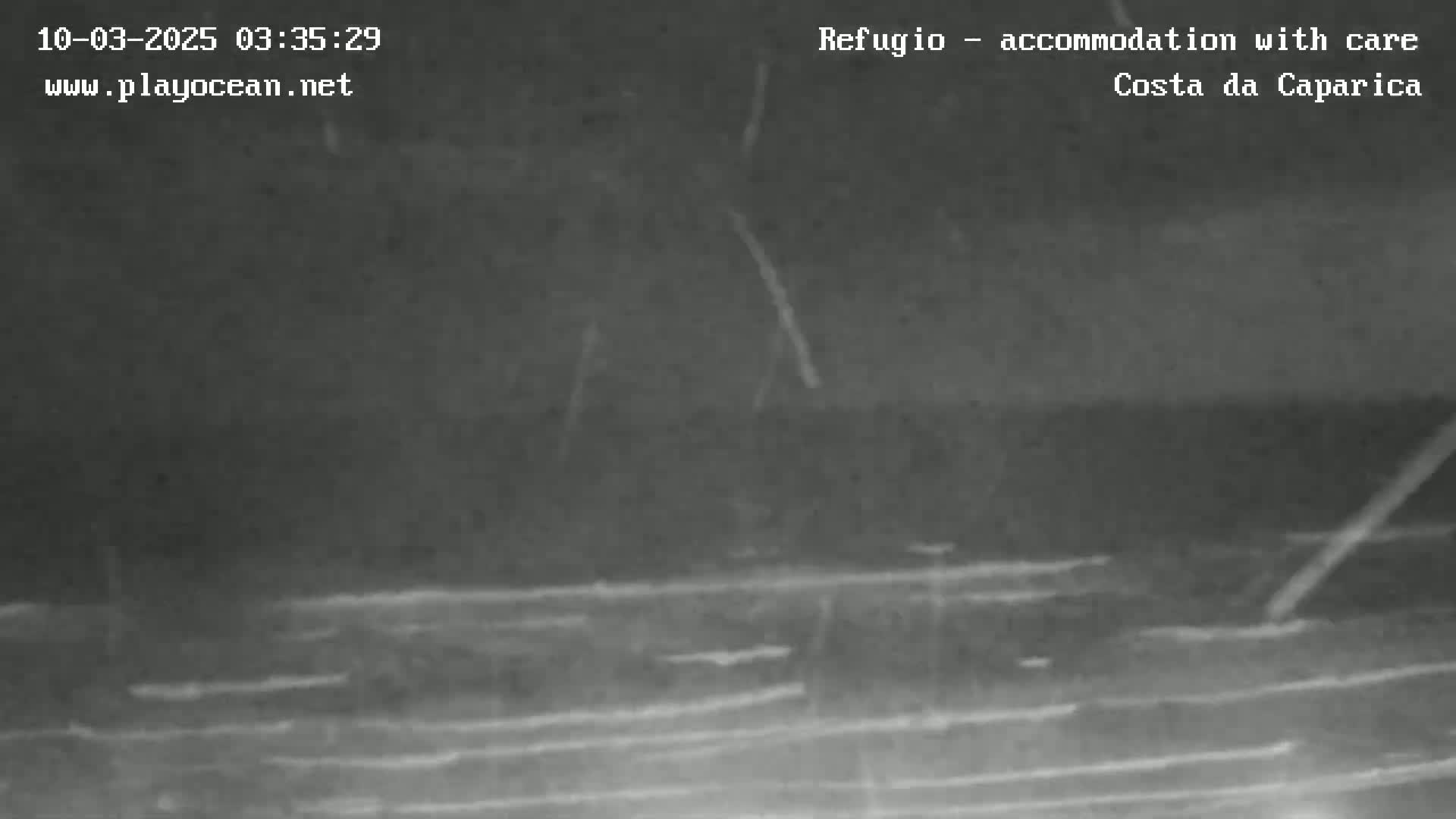 A nighttime, low-light image shows dark, wavy water under a dark sky with streaks of light possibly from rain or other precipitation.