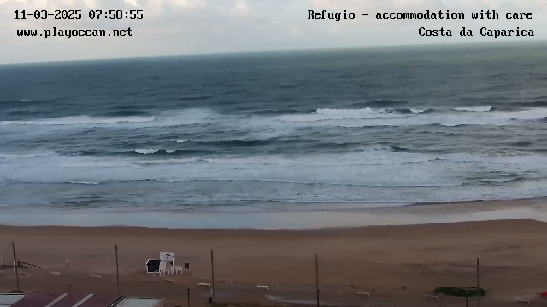 A mostly cloudy day shows an expansive view of a beach with moderate waves rolling onto the shore.
