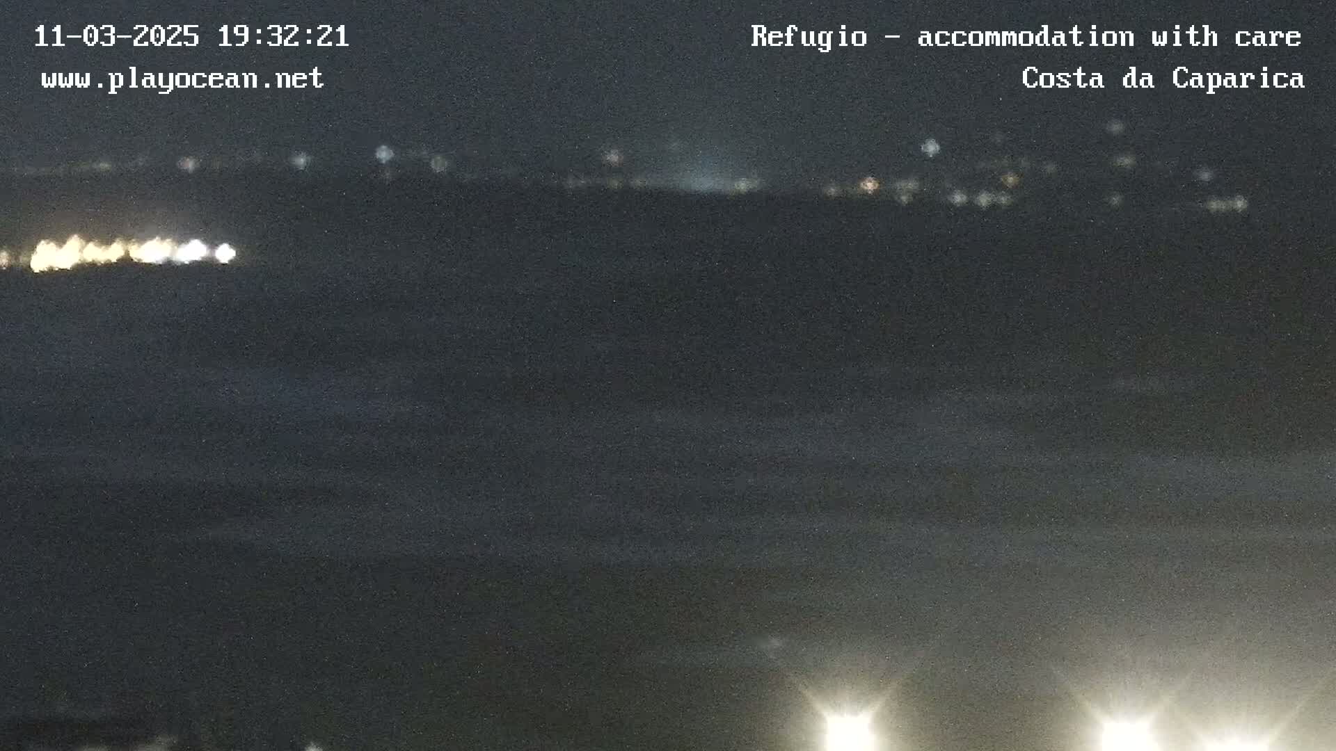 A nighttime, dark view of a shoreline with distant lights from a town or city across a body of dark water.