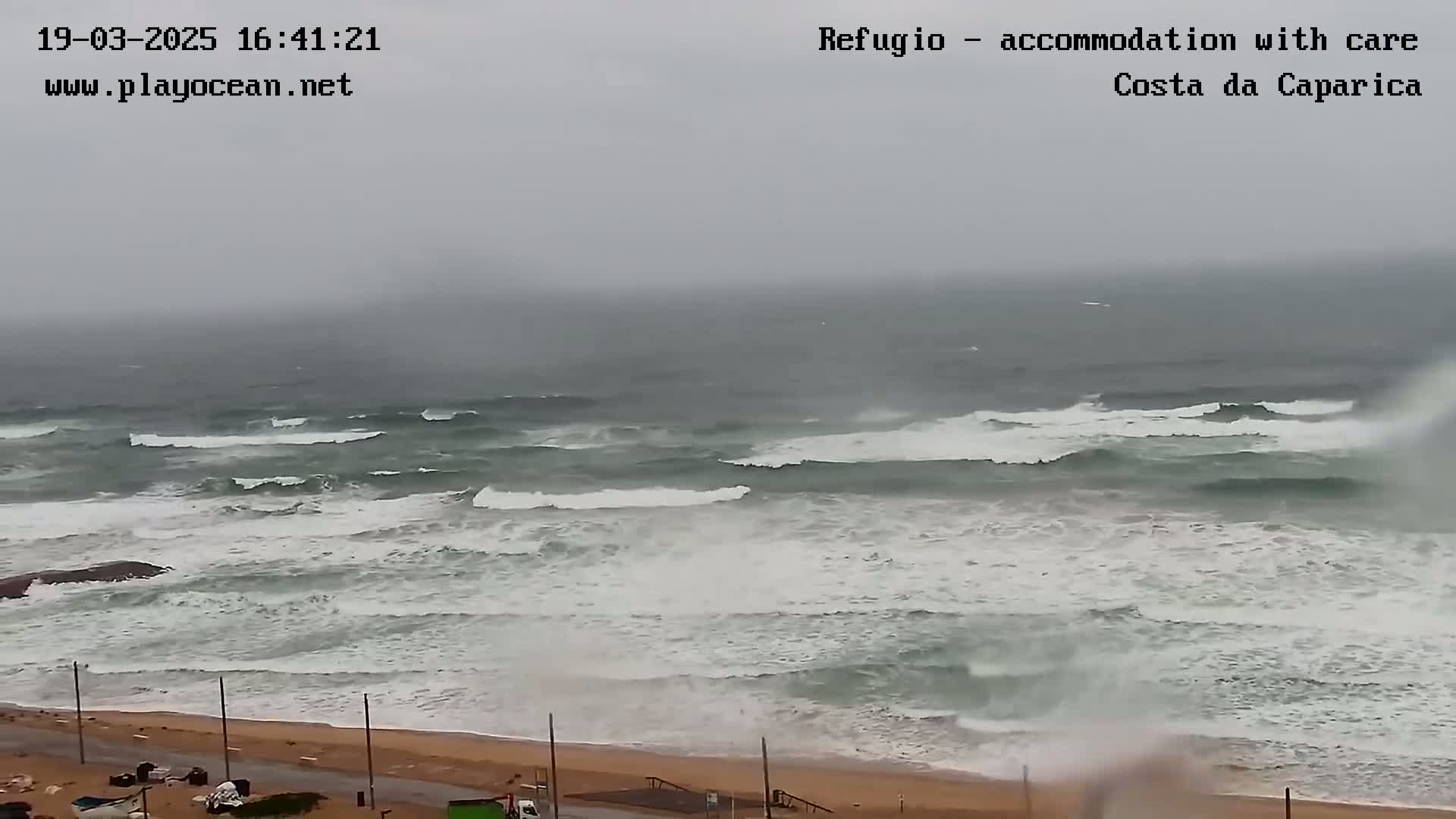A beach with stormy gray skies and large waves crashing onto the shore.