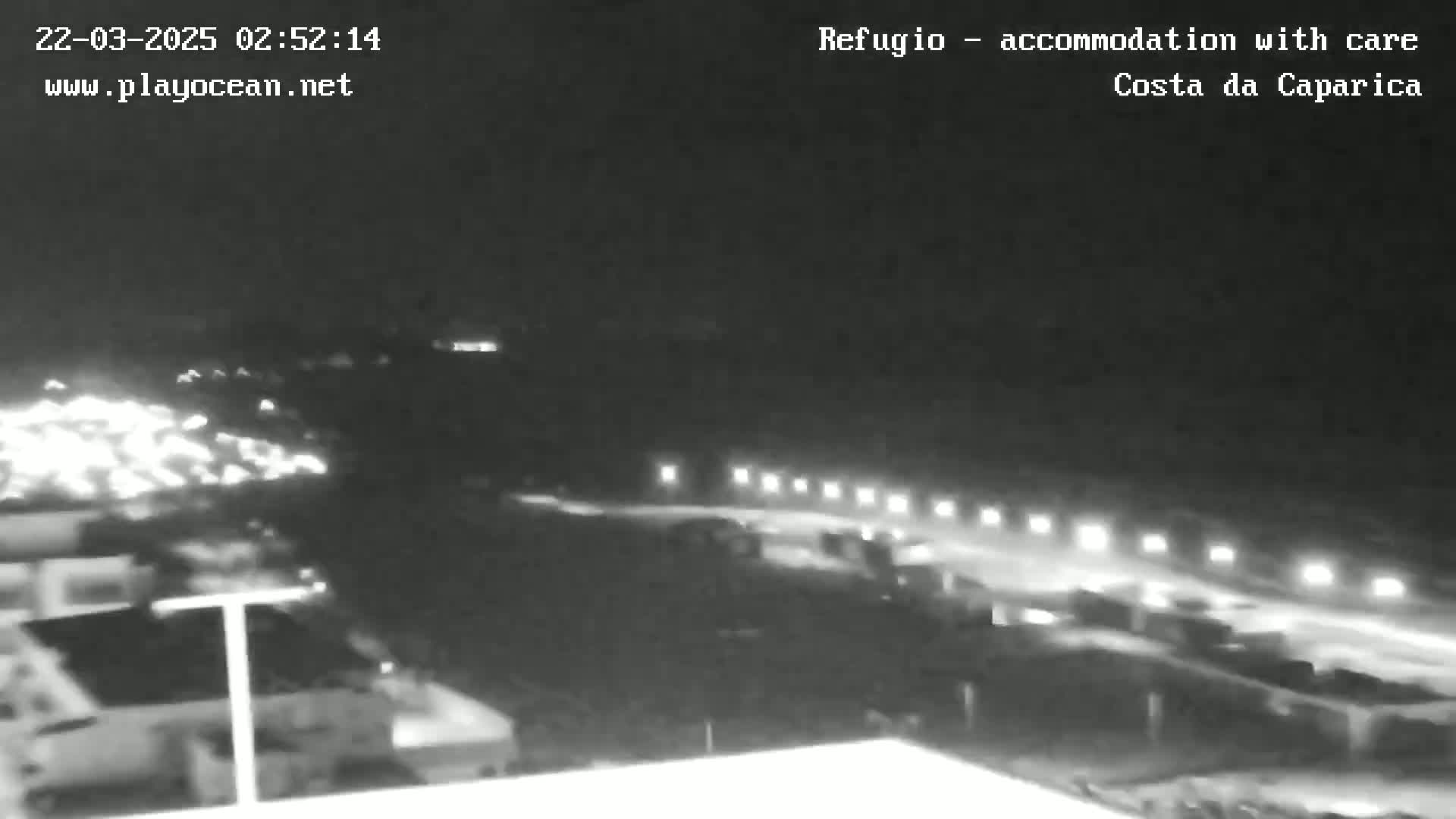 A nighttime, low-light view shows a parking lot with several cars and a roadway with lights extending into the distance.