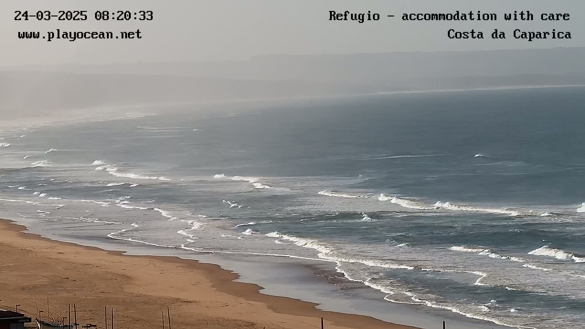 A hazy, expansive ocean view shows waves rolling onto a sandy beach.