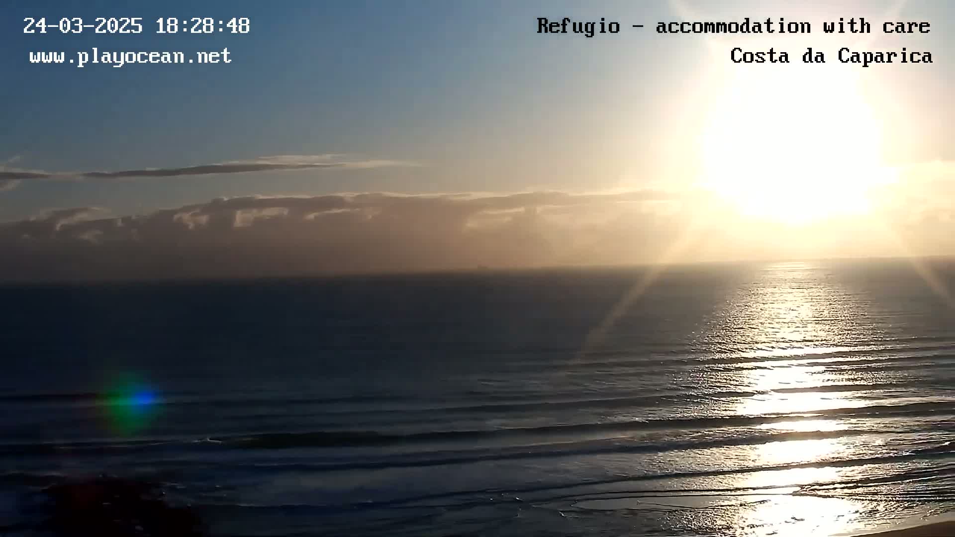 A bright sun sets over a dark ocean with small waves, under a partly cloudy sky.