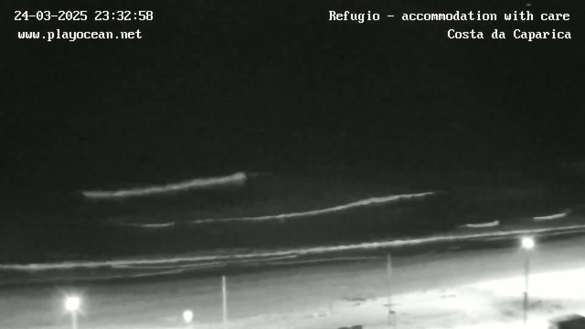 A nighttime, low-light beach scene shows dark, wavy ocean water under a mostly clear sky with some faint, high clouds.