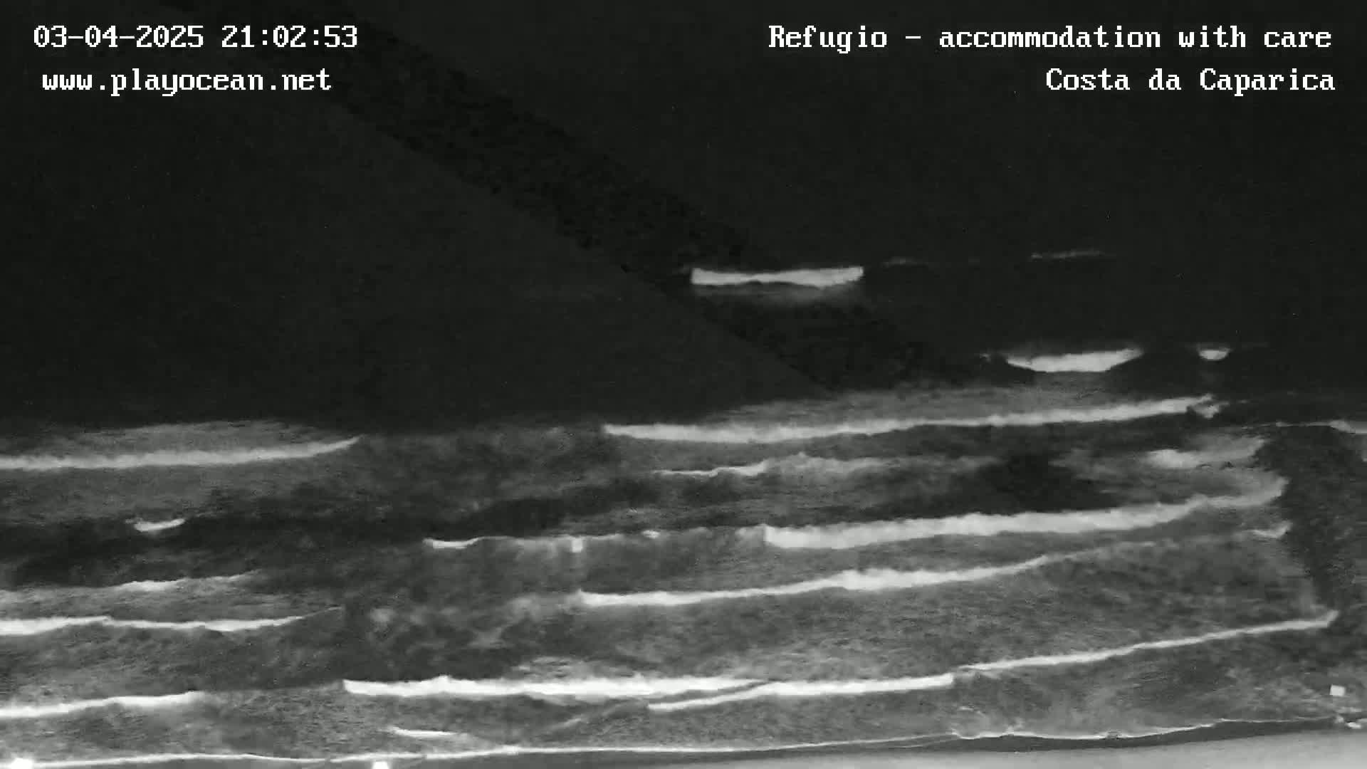 A nighttime, low-light image shows several lines of waves rolling onto a dark shoreline.