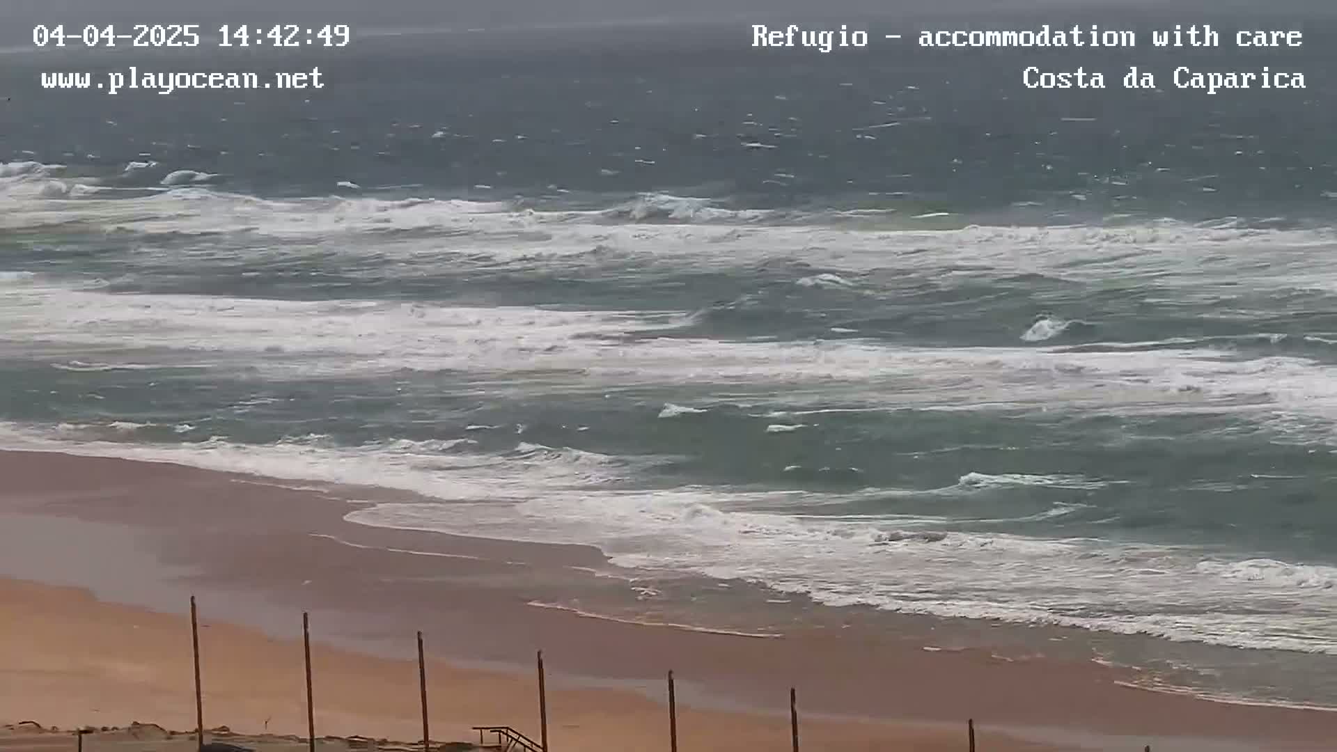 A sandy beach meets a choppy, gray-green ocean under an overcast sky.