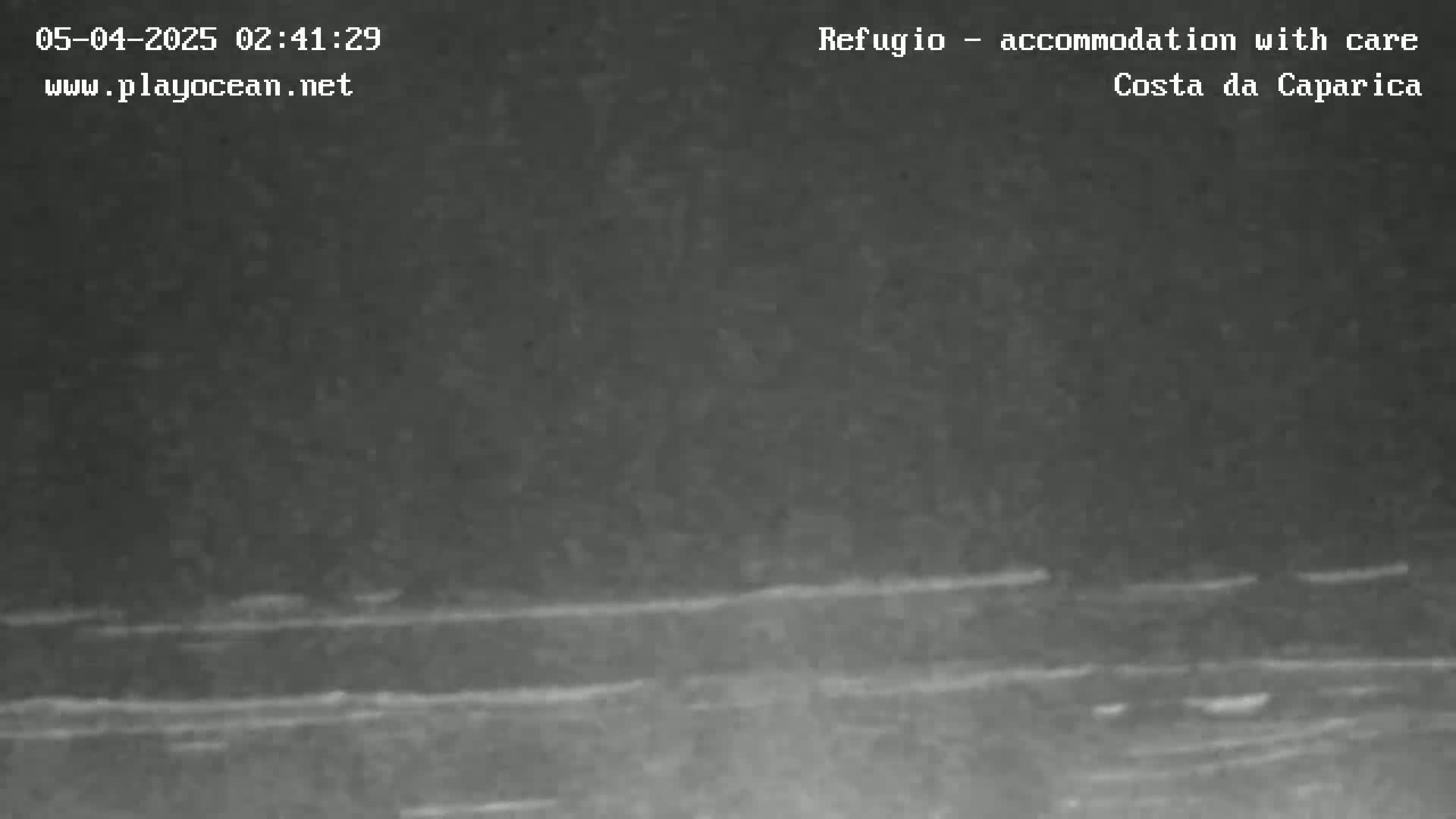 A low-light, nighttime image shows a dark, seemingly calm body of water with faint horizontal lines suggesting waves or reflections.