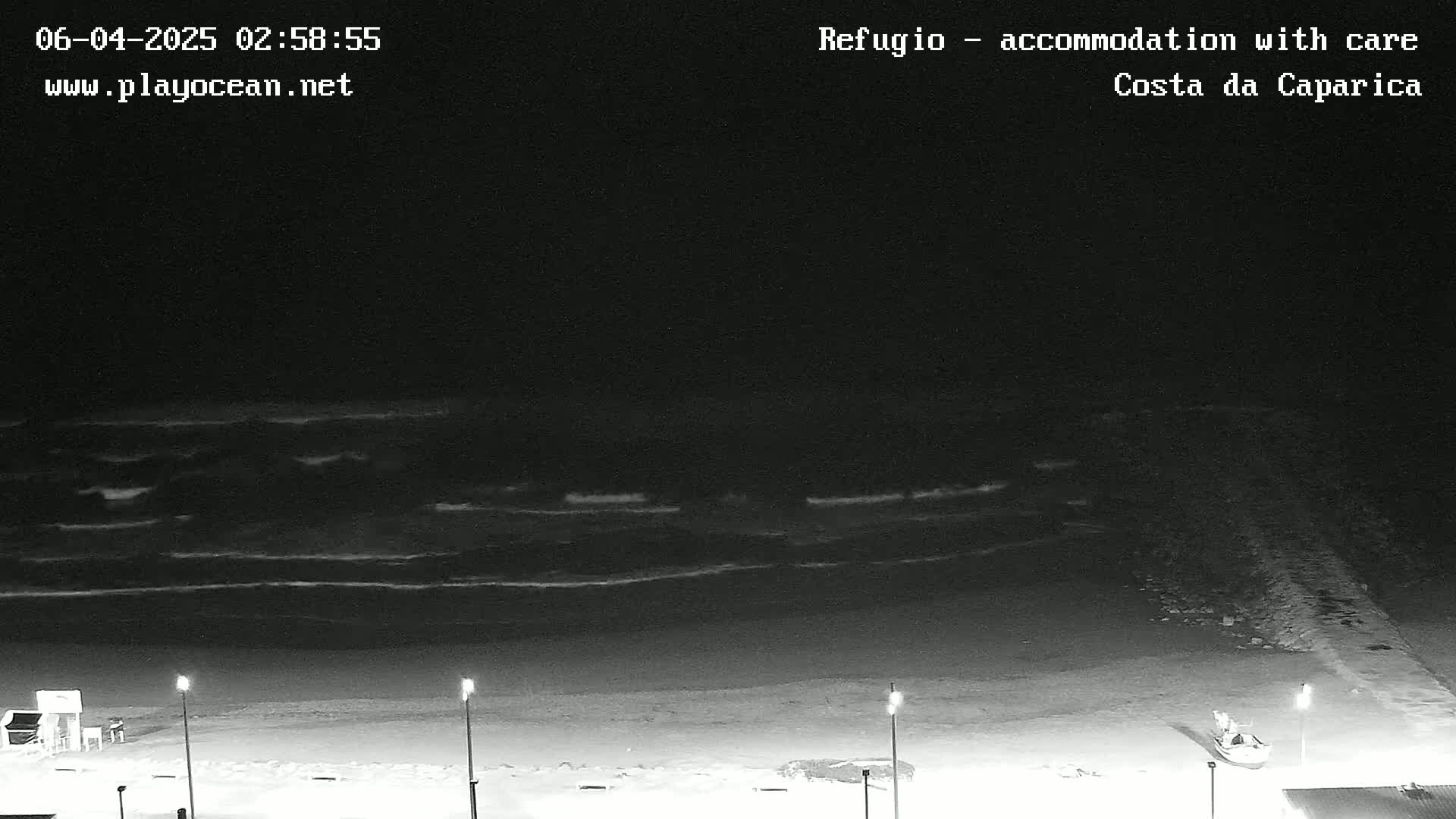 A nighttime view of a dark beach with gently rolling waves under a clear, black sky.