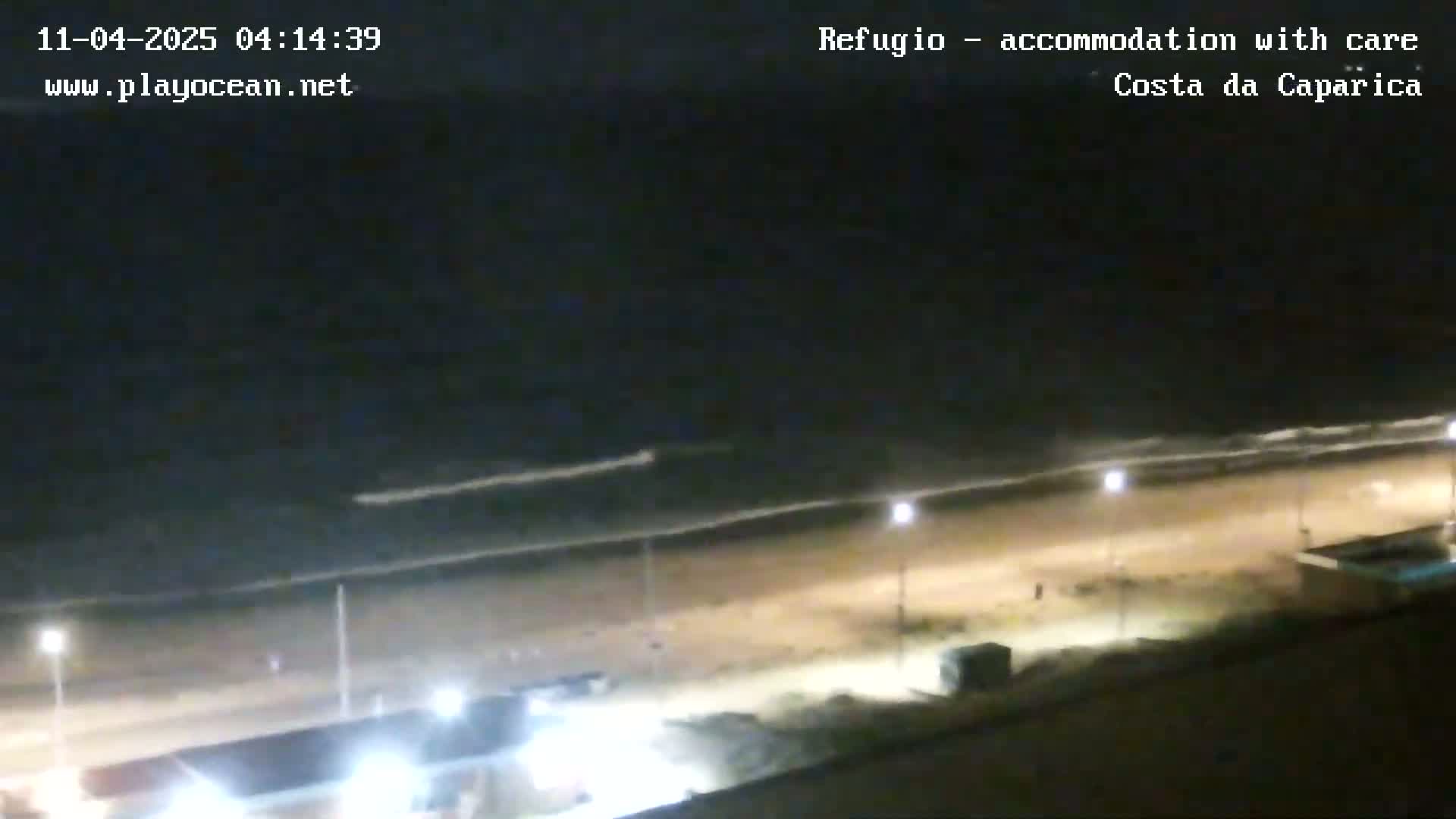 A nighttime view of a mostly empty beach with gently lapping waves under a dark sky.