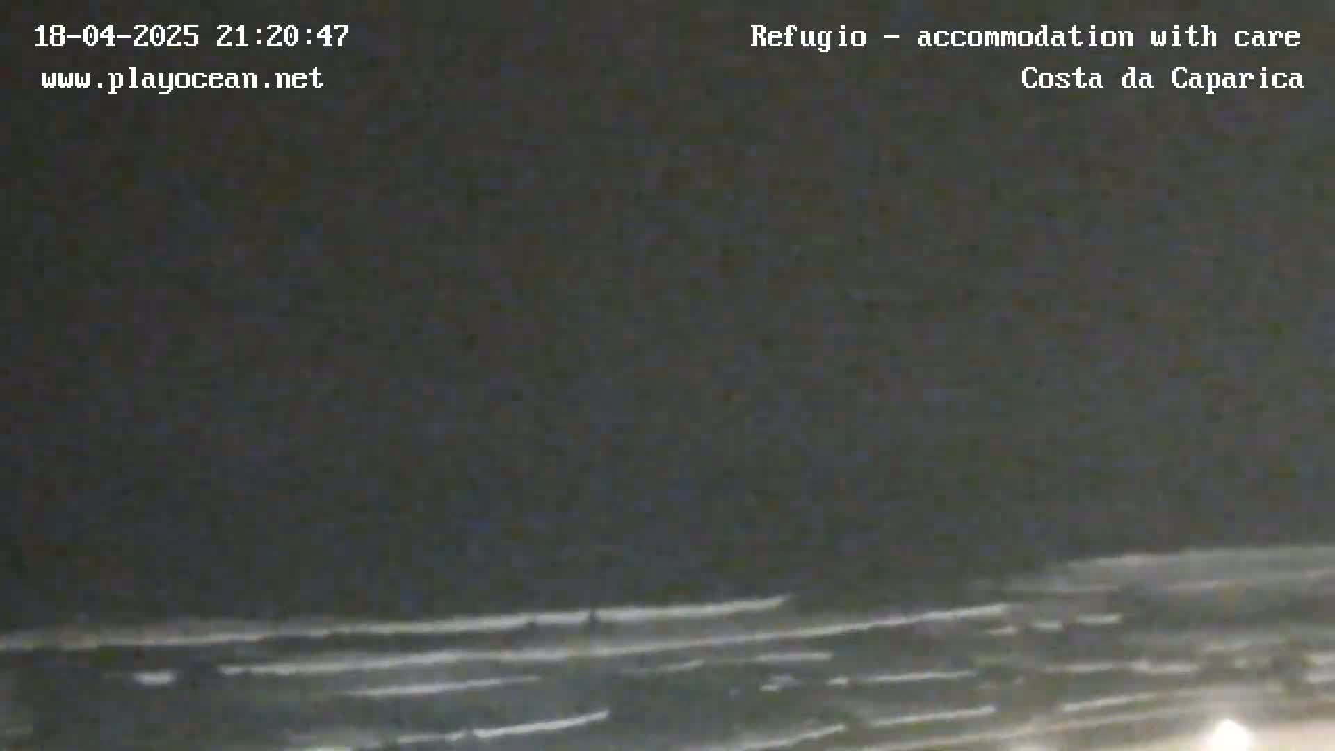 A nighttime, low-light view of a dark ocean with faintly visible waves under a cloudy sky.