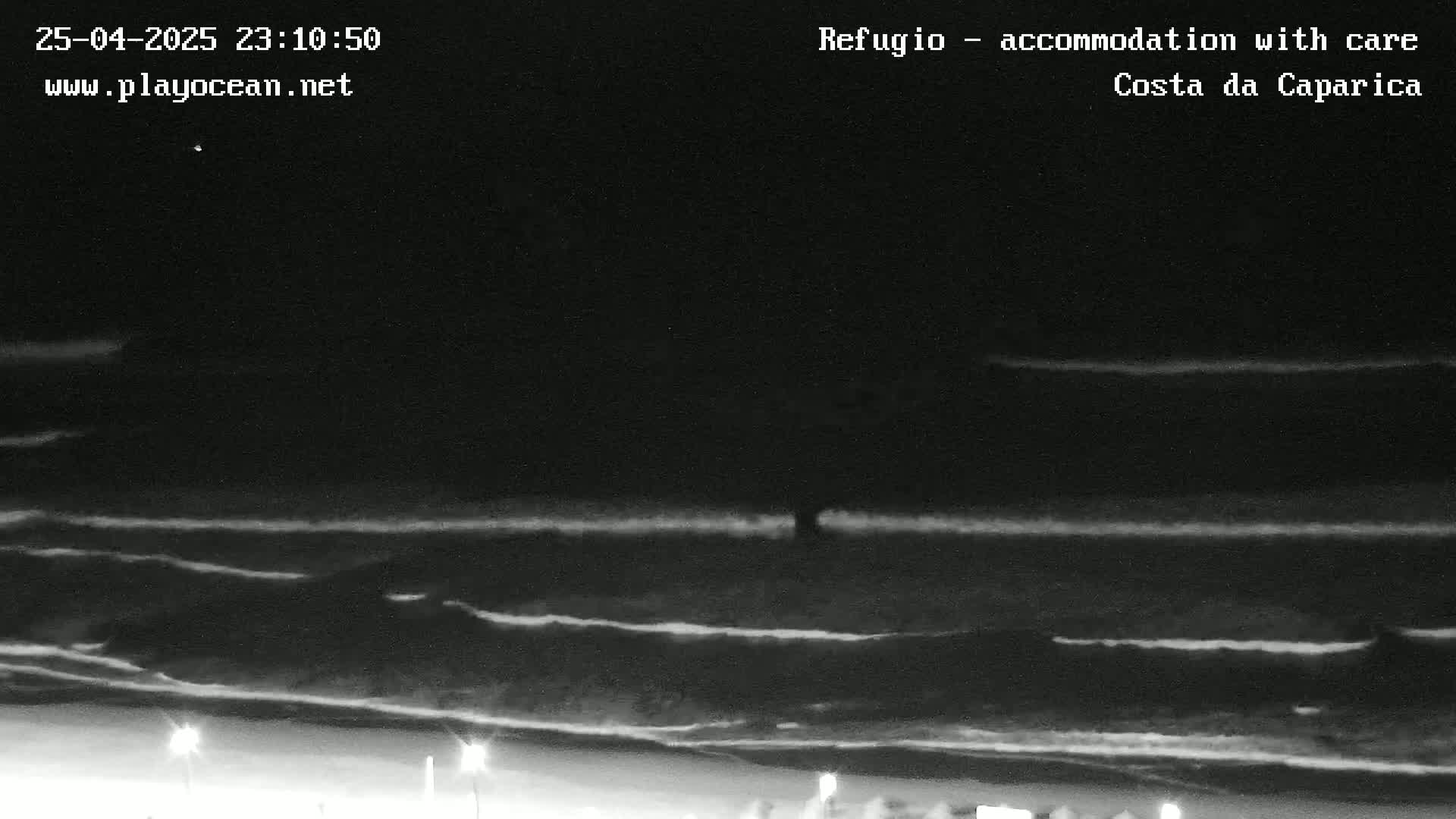 A nighttime, low-light image shows dark ocean waves lapping a beach under a mostly clear, dark sky.