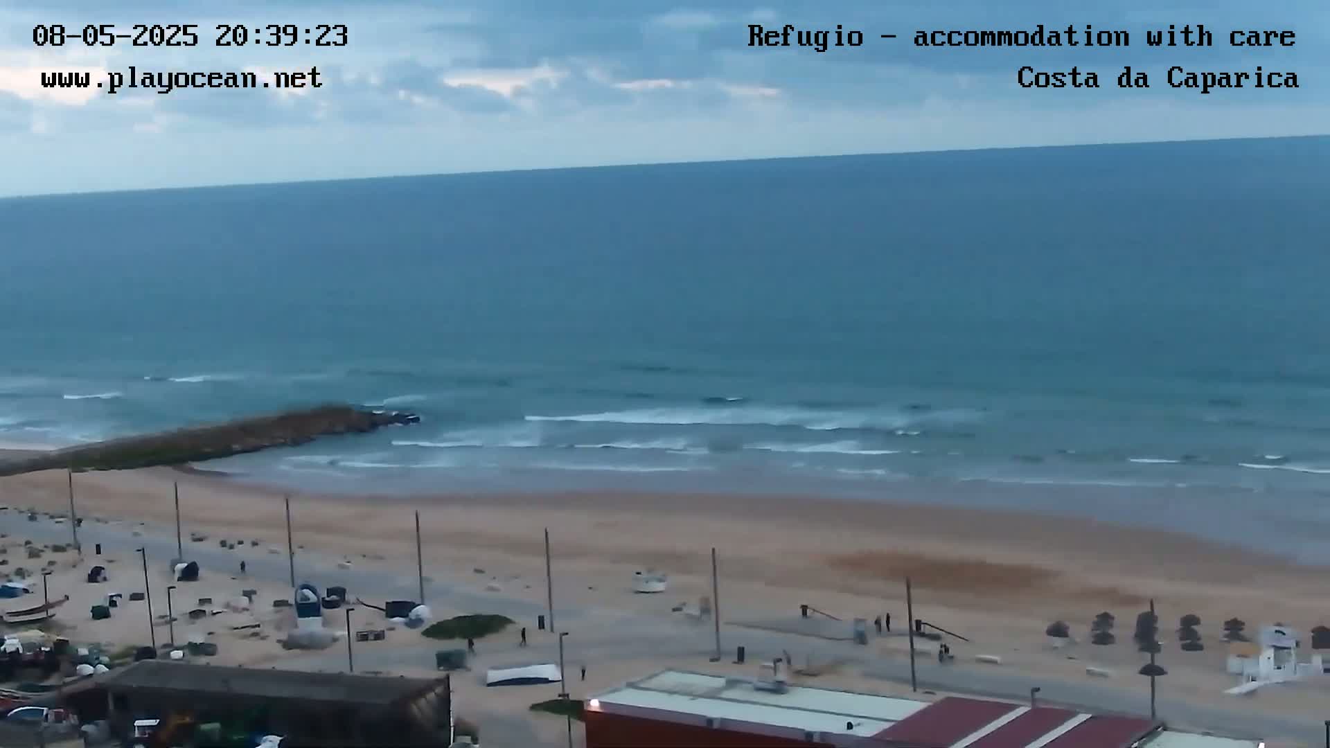 An overcast sky looks down on a mostly empty beach with calm waves gently rolling ashore.