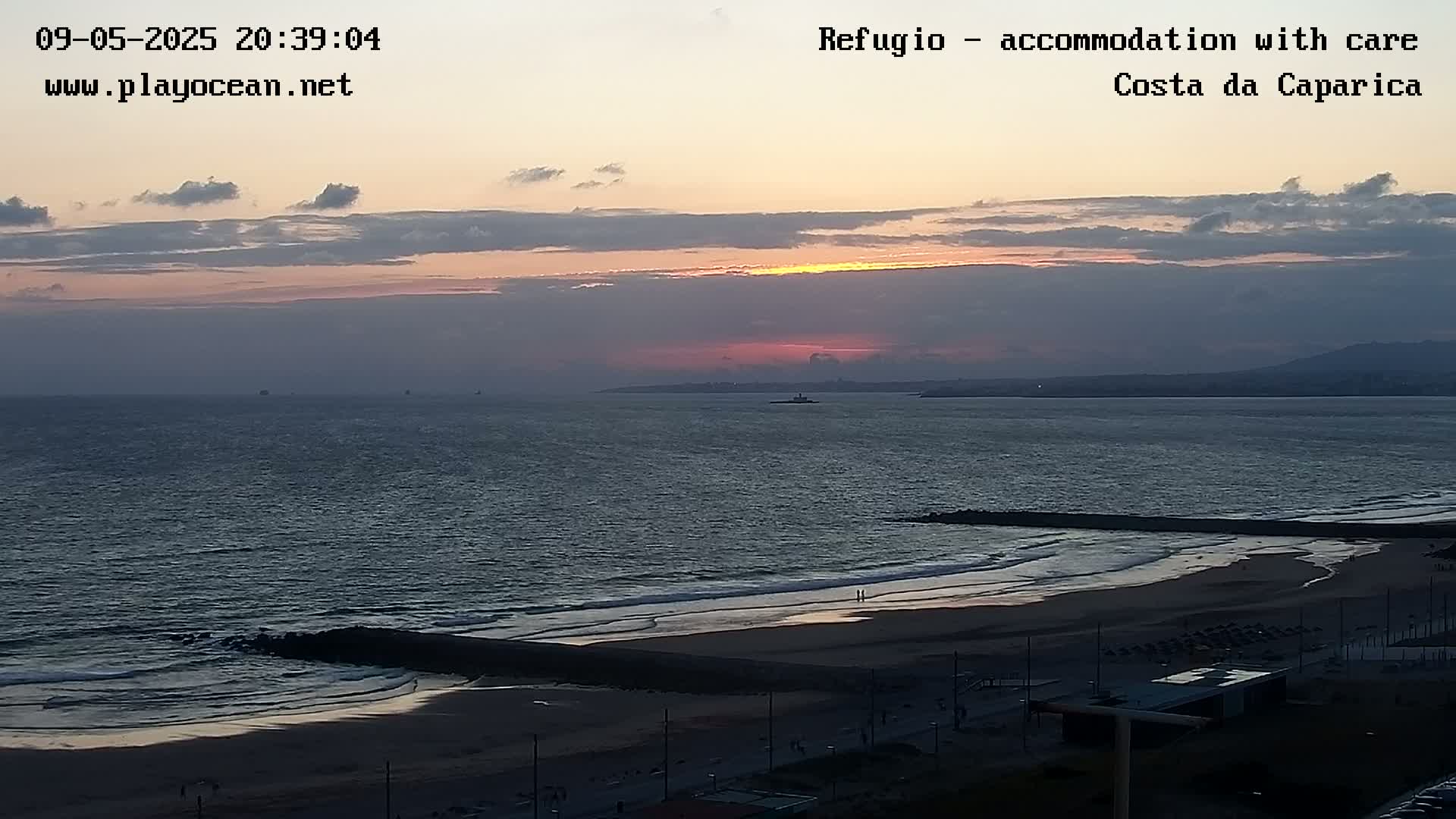 A beach at sunset, with calm waves gently lapping the shore under a mostly cloudy sky.