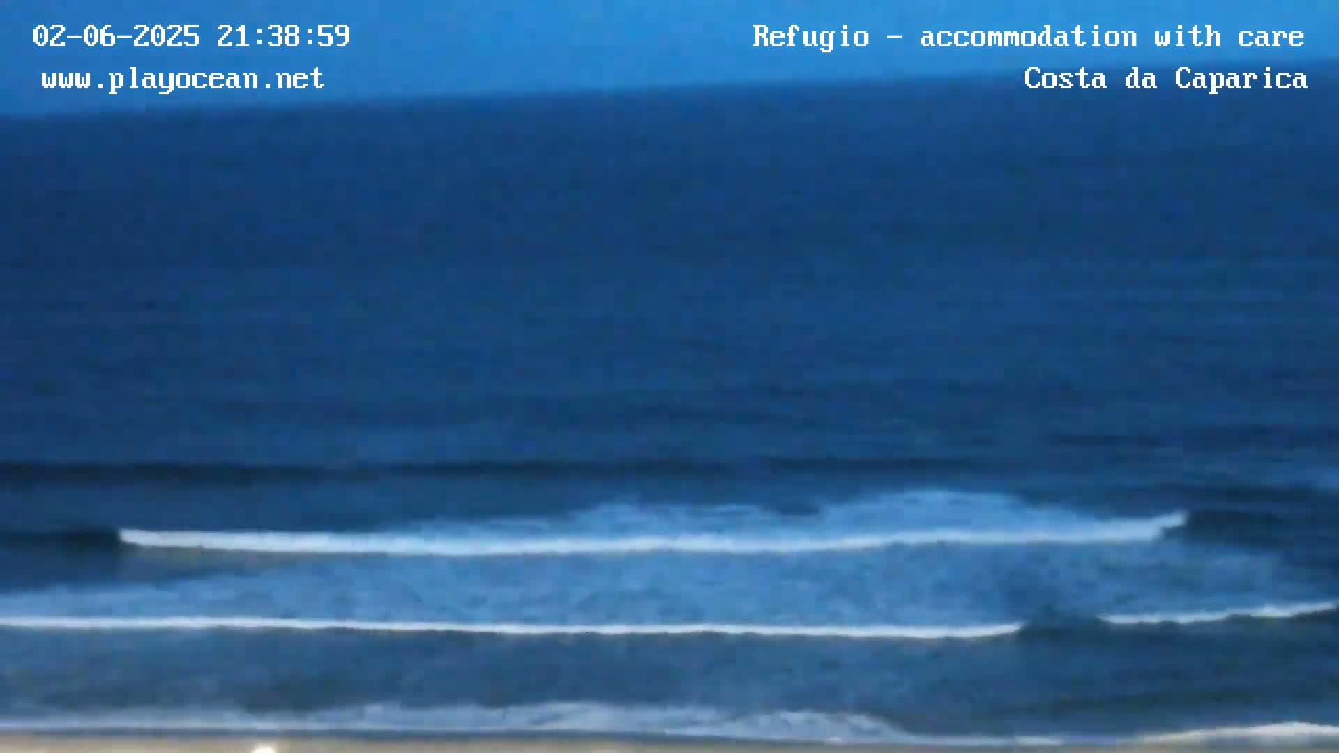 A dark blue ocean with small waves rolls onto a sandy beach under a twilight sky.