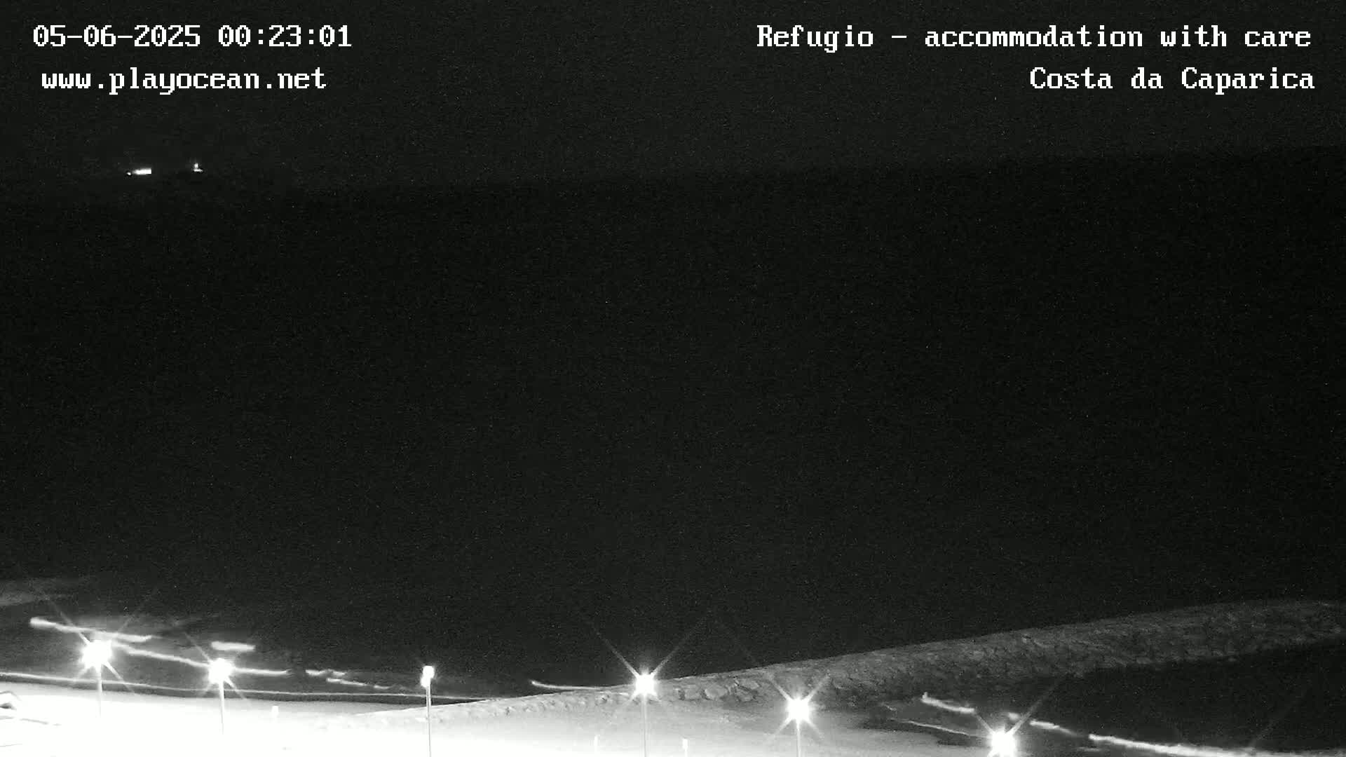 A nighttime, low-light view of a dark coastline with a few lights visible on the shore.