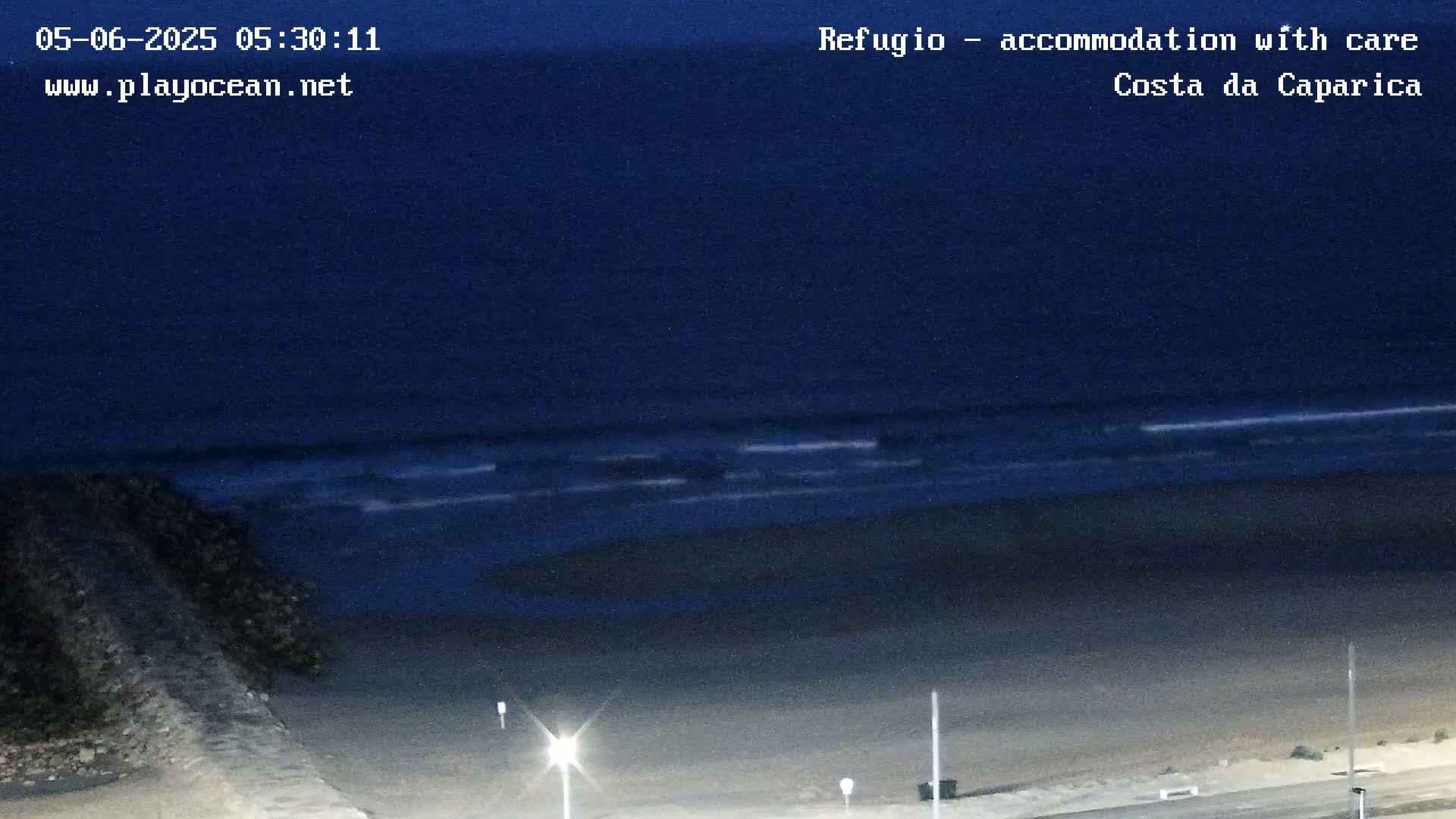 A dark beach at night is seen from above, with gently rolling waves visible in the dark ocean.