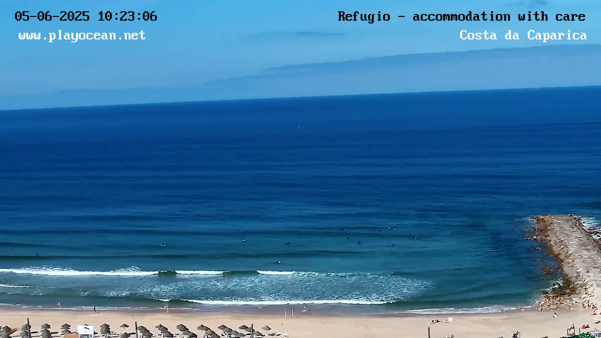 A sandy beach with several surfers in the ocean on a sunny day.