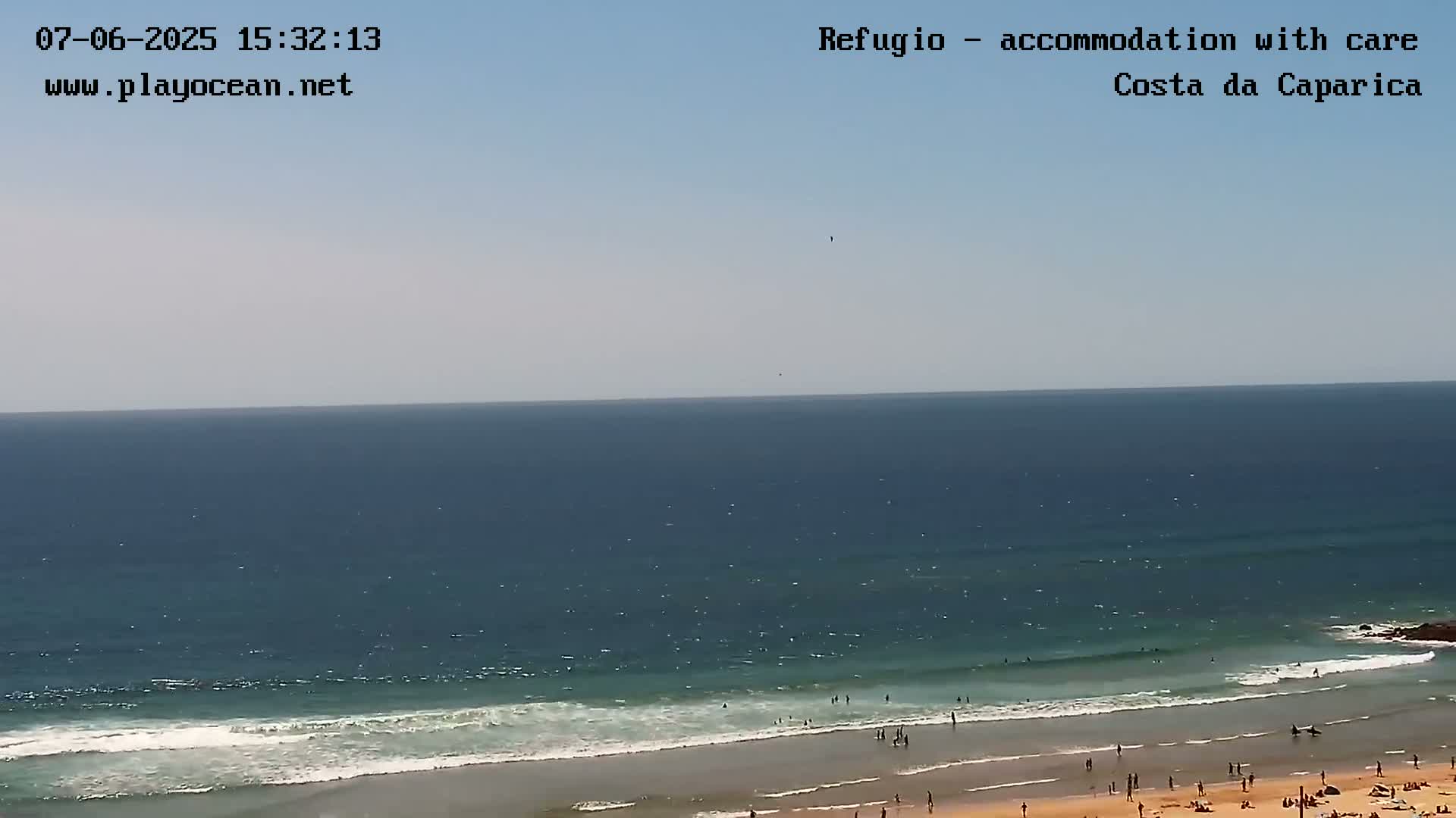 A mostly sunny day shows a beach with people swimming and sunbathing, gentle waves rolling into shore, and a calm ocean extending to the horizon.
