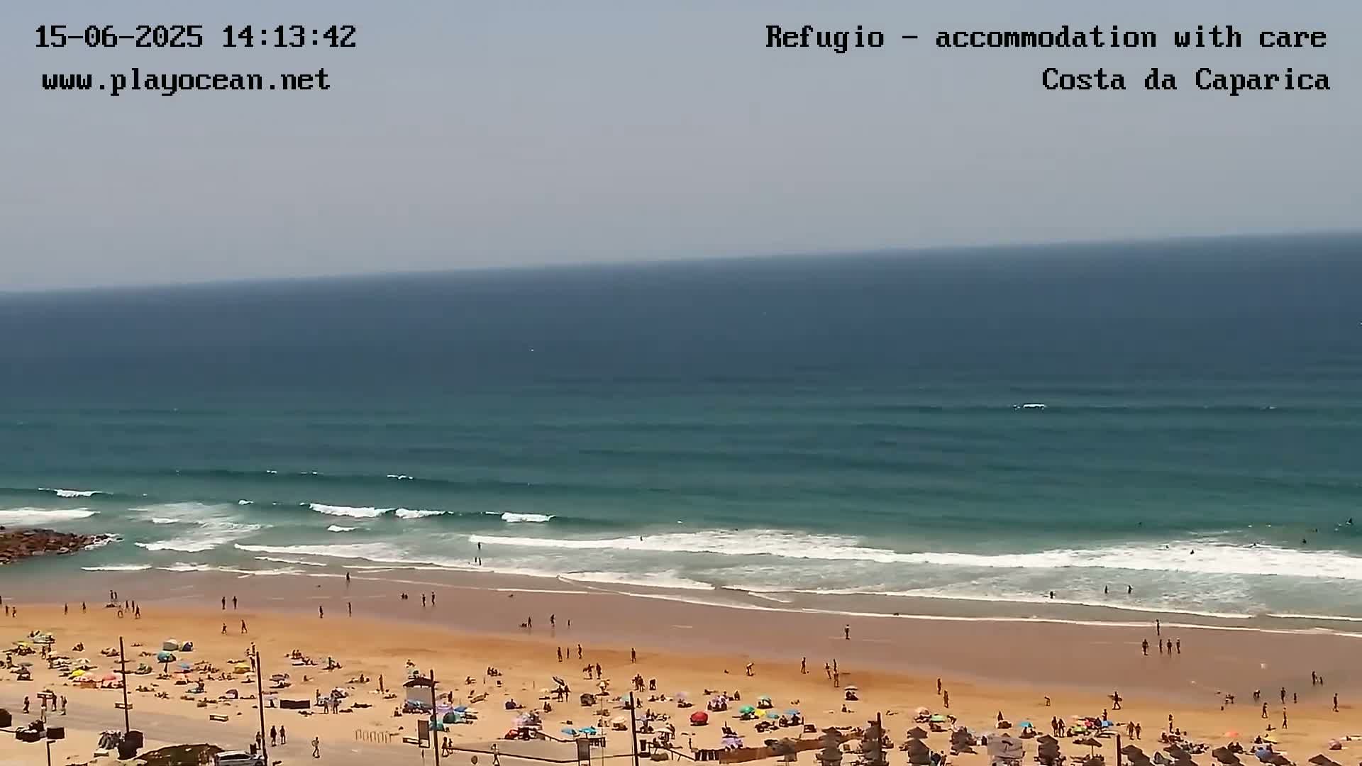 A sandy beach with many people sunbathing and swimming is met by gentle ocean waves on a partly sunny day.