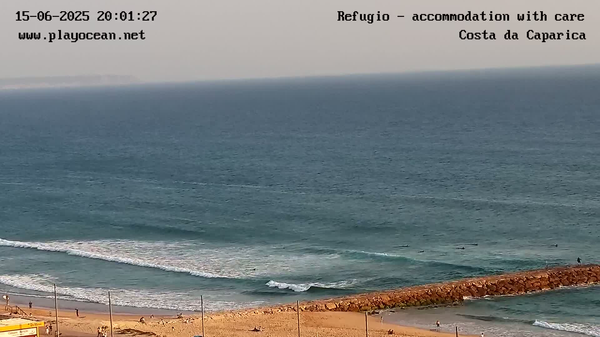 A sandy beach with many people sunbathing and swimming is met by gentle ocean waves on a partly sunny day.