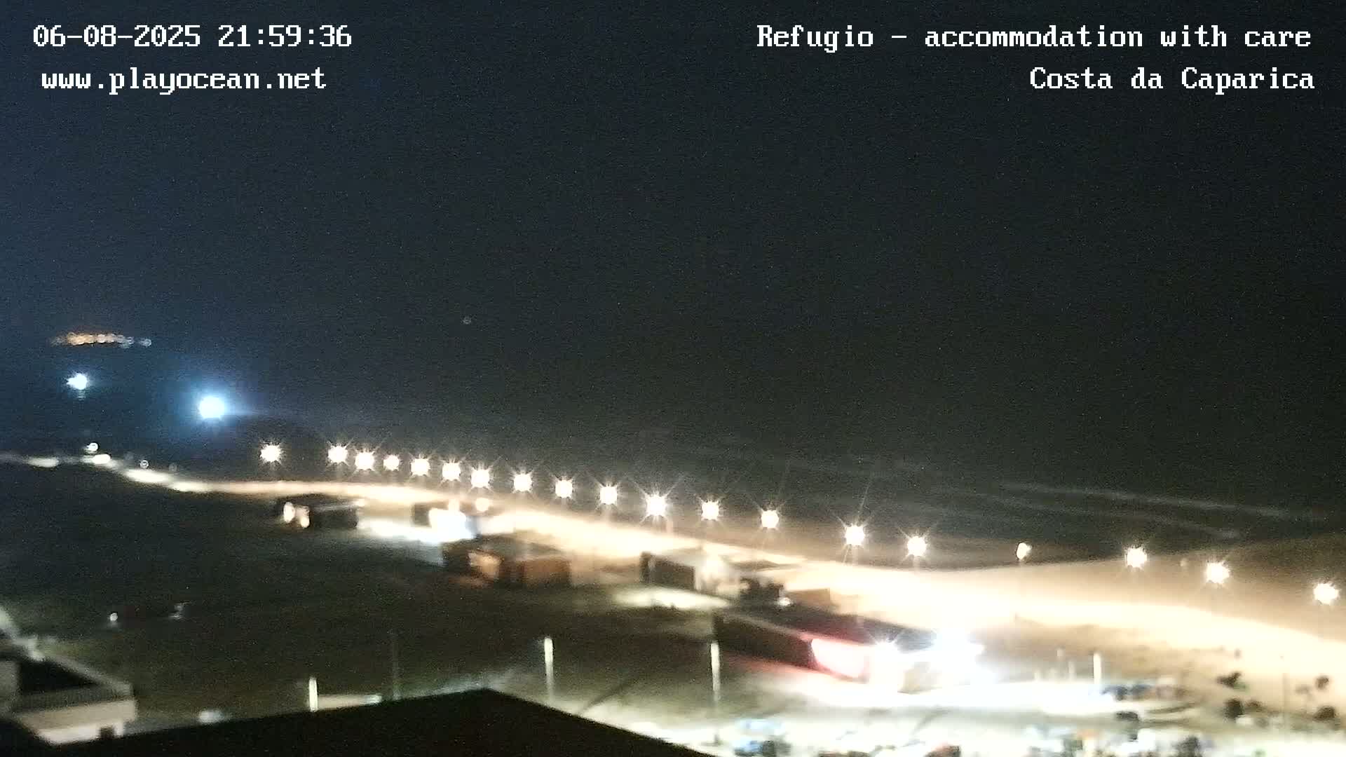 A nighttime, beachside view shows a row of lights illuminating a sandy beach and ocean waves under a dark sky.