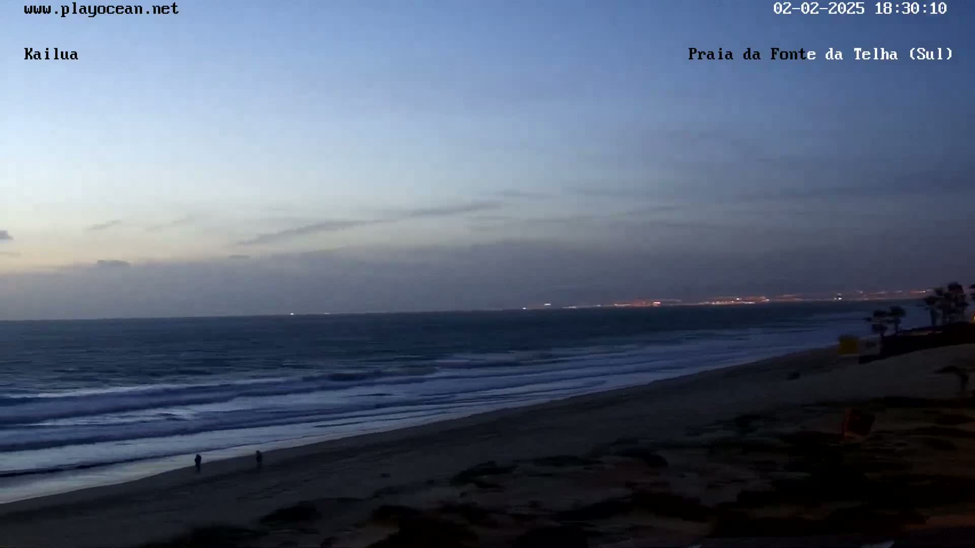 A dark beach with gently rolling waves under a twilight sky.